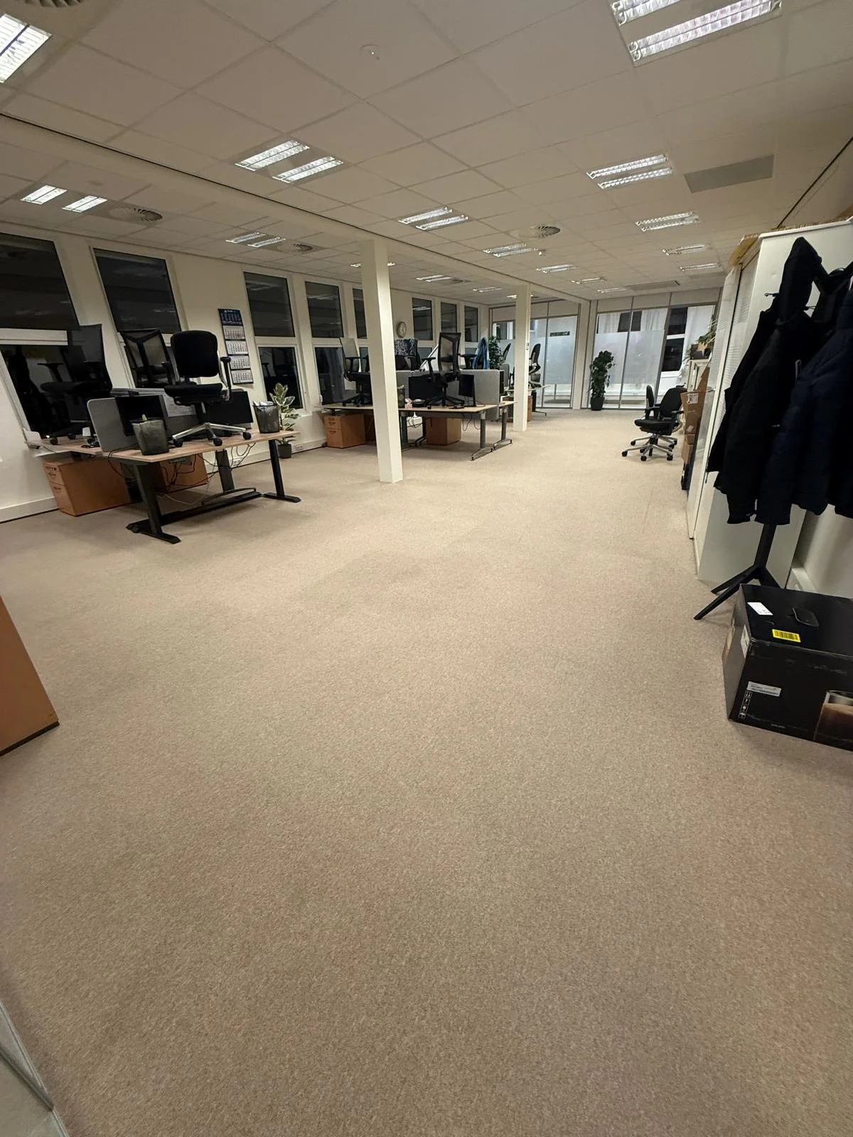Kantoorruimte met bureaus, bureaustoelen en vloerbedekking.