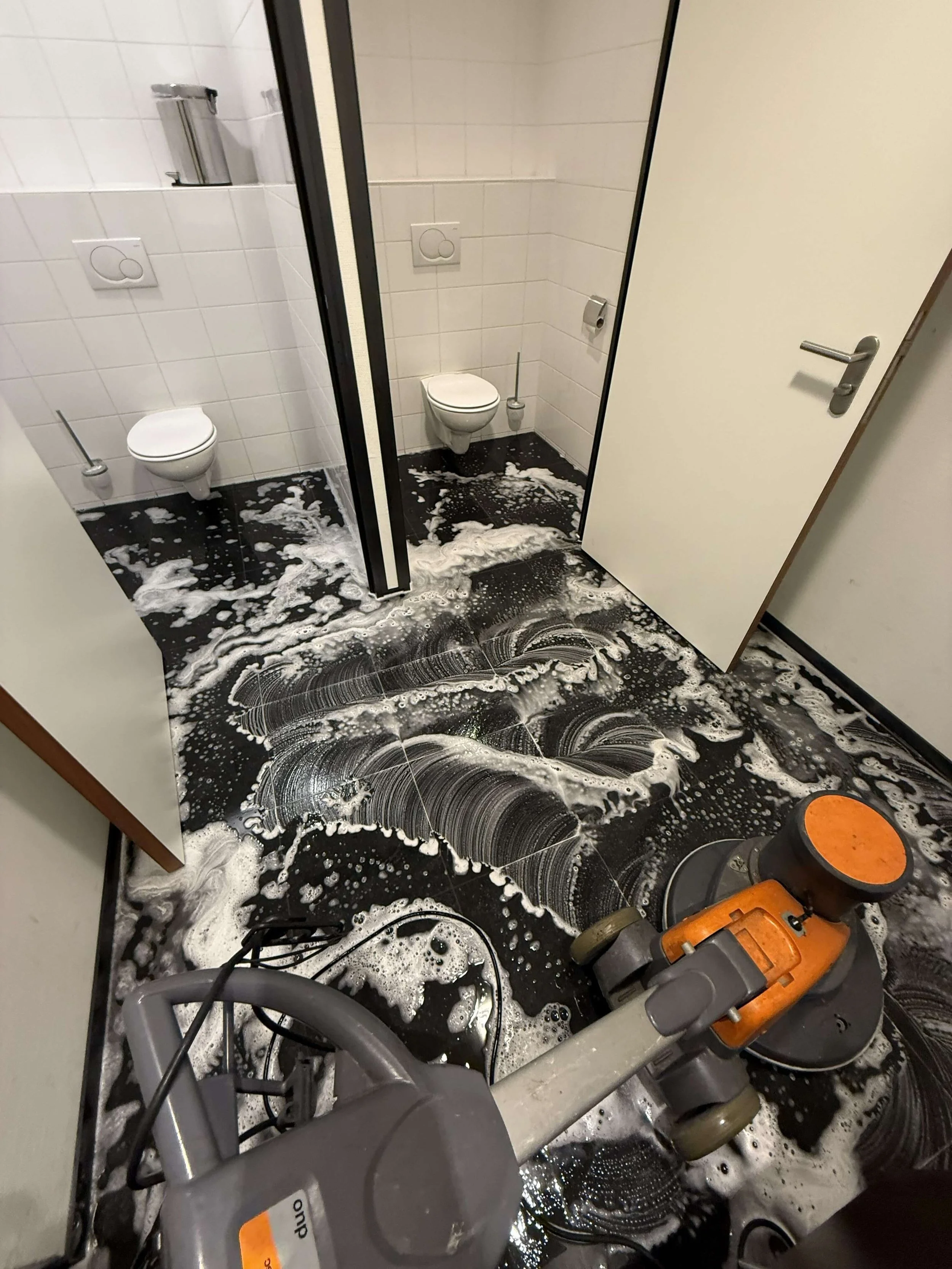 Machinale reiniging van een betegelde vloer in een sanitaire ruimte.