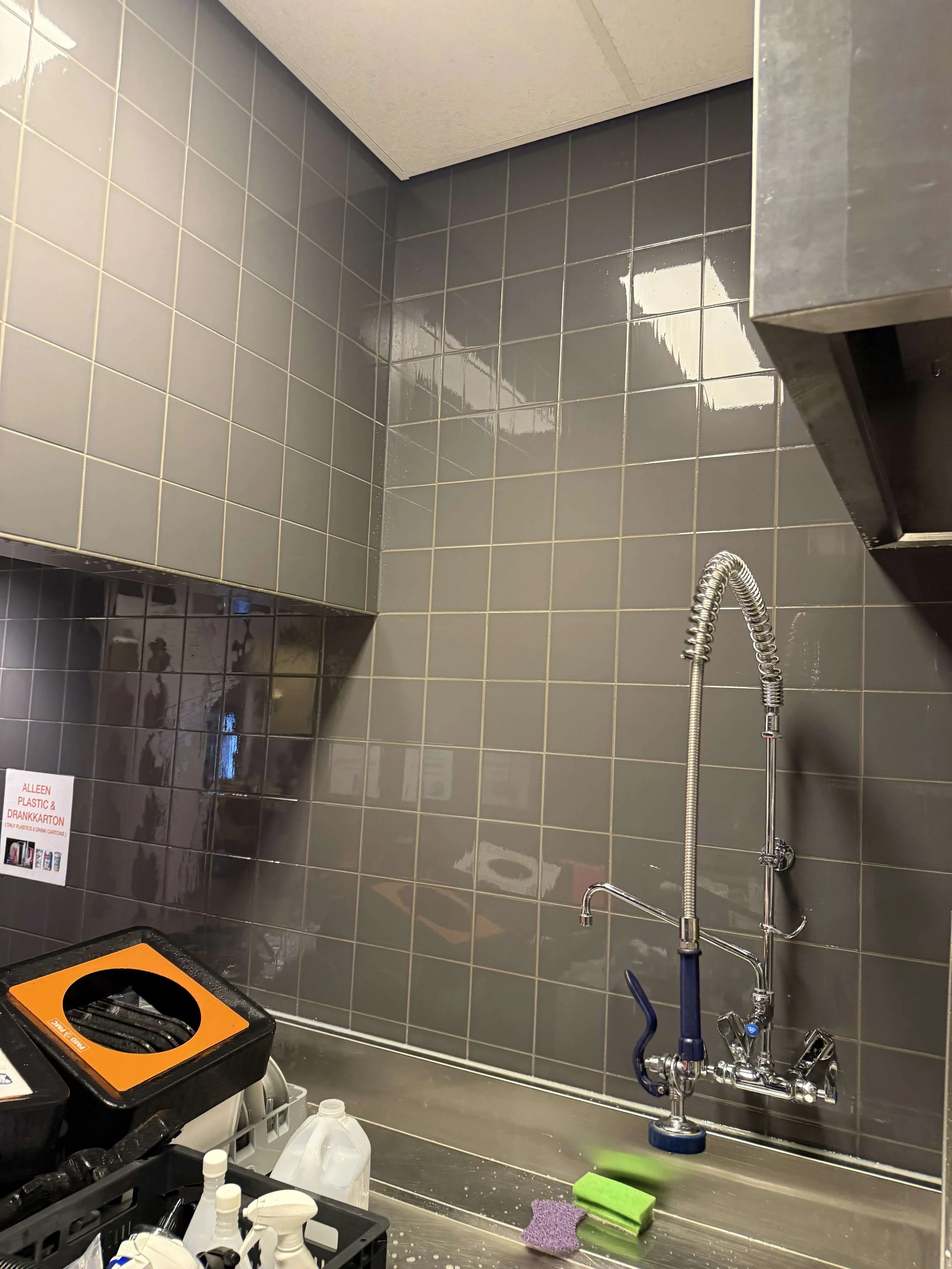 Betegelde wand met spoelkraan en afzuigkap in een professionele keuken.