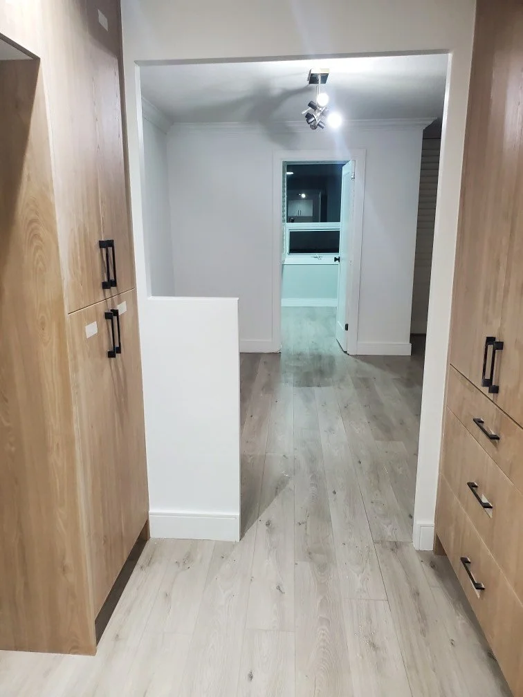 Interior of a modern hallway with wooden cabinets and laminate flooring leading to a room with a door and ceiling lights.