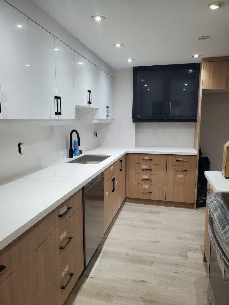 Modern kitchen with white cabinets, wood finish lower cabinets, stainless steel dishwasher, a sink with black faucet, and recessed ceiling lights.
