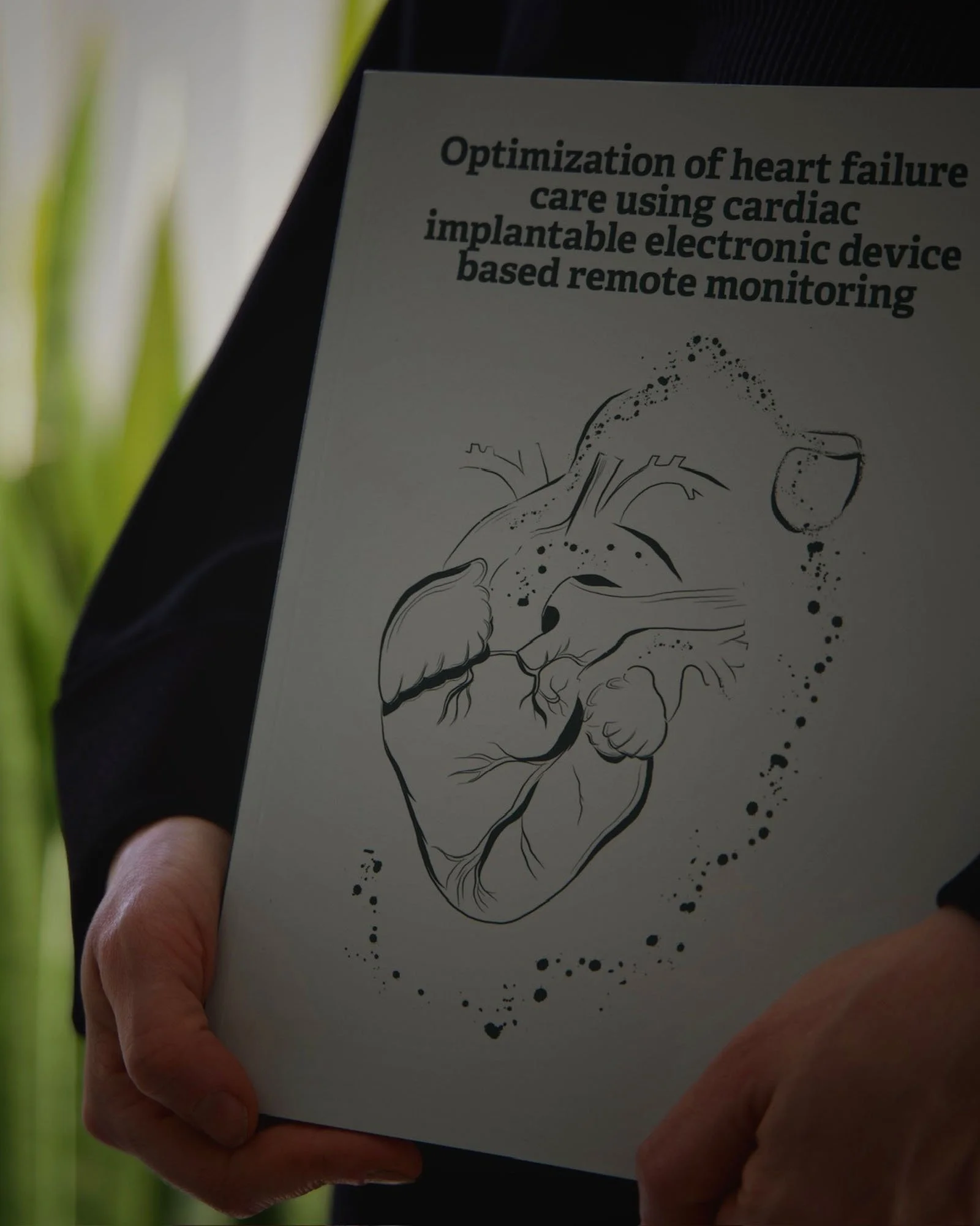 Hand holding a paper with a line drawing of a human heart and a headline about heart failure care using a cardiac implantable electronic device for remote monitoring.