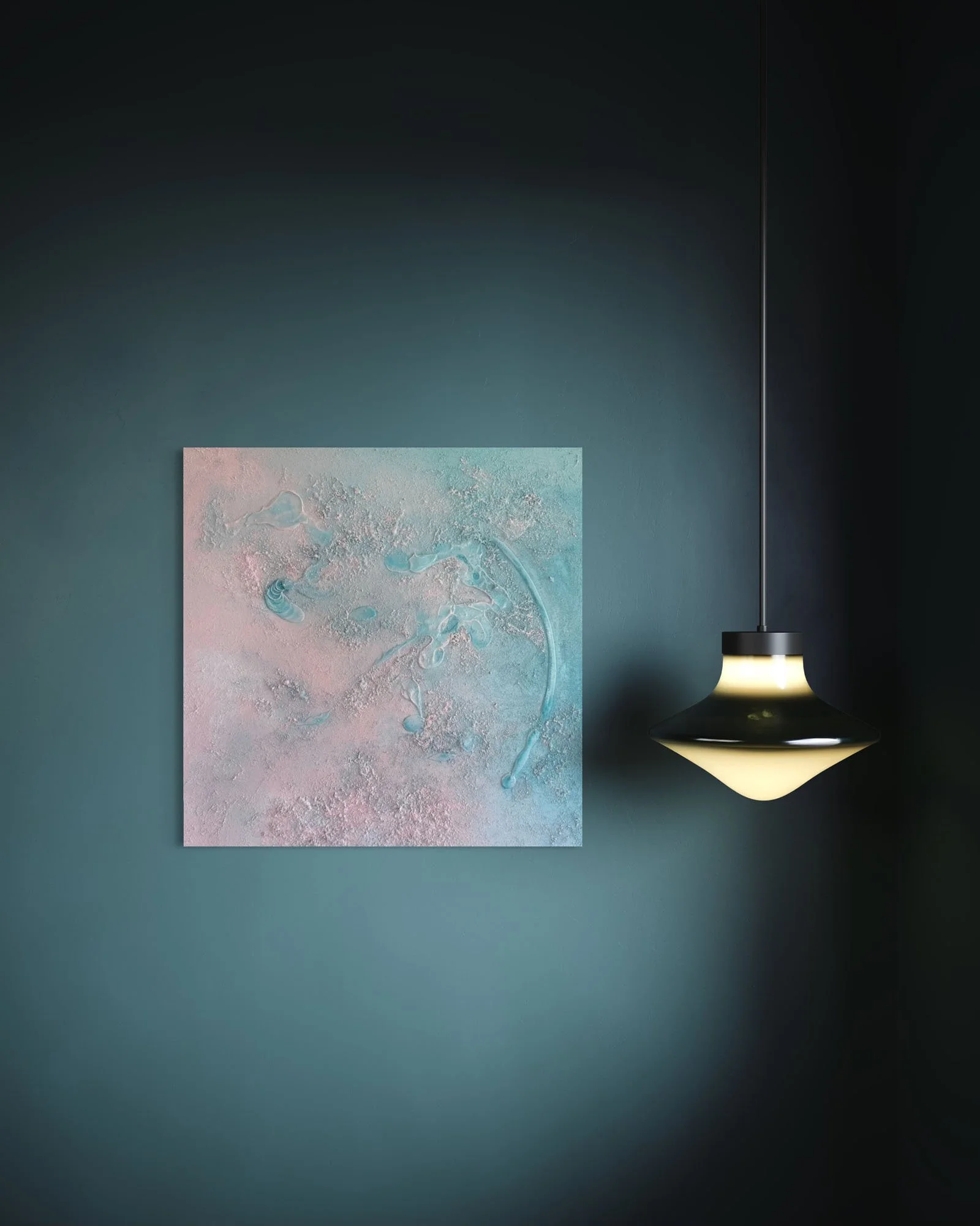 A framed abstract textured painting with pastel colors hanging on a dark teal wall, illuminated by a modern ceiling pendant light.