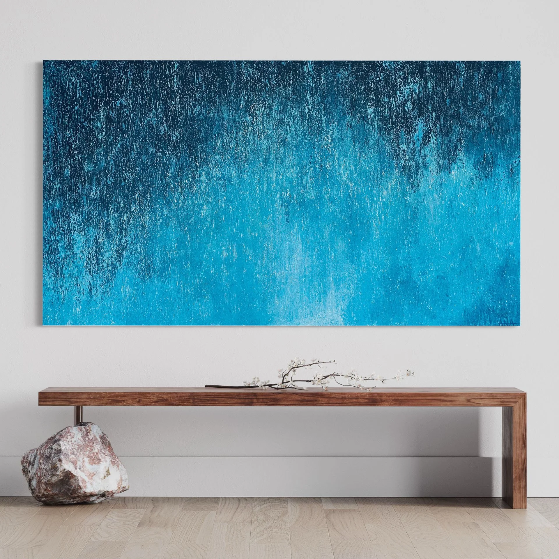 Modern interior with a large abstract blue painting on the wall, a wooden console table, a branch with blossoms, and a large stone or coral on the floor.