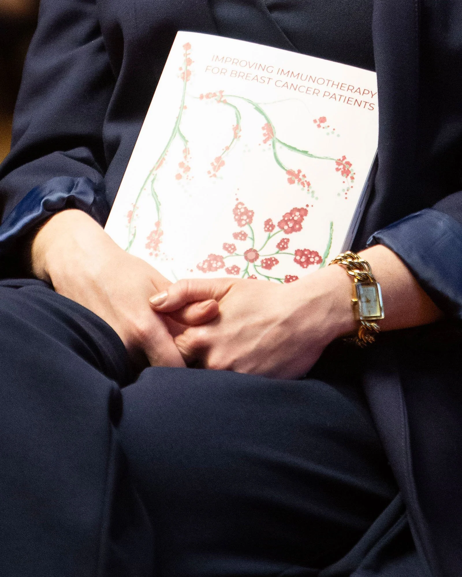 A person holding a booklet titled 'Improving Immunotherapy for Breast Cancer Patients' with a floral design on the cover.