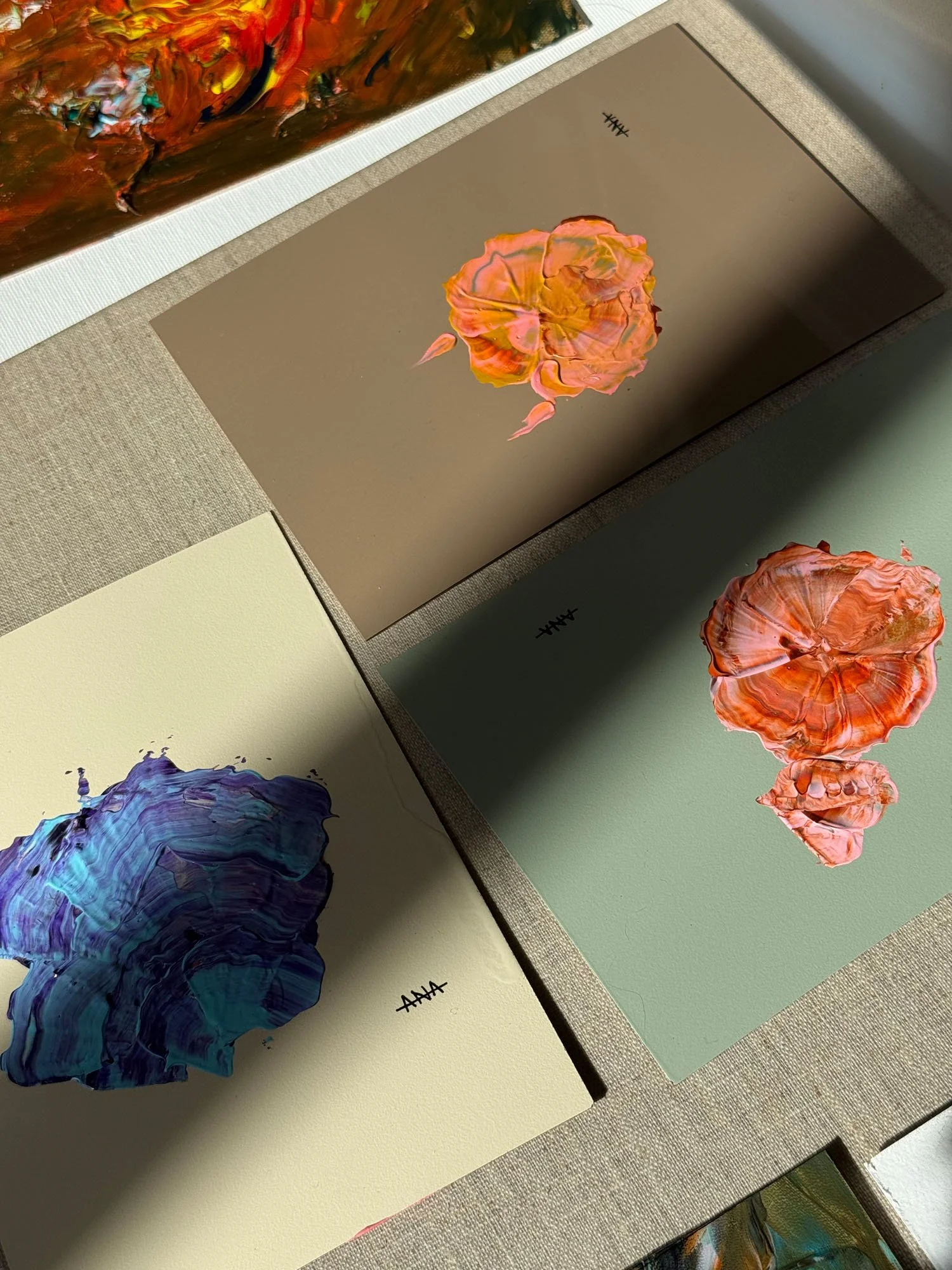 Close-up of abstract paintings featuring textured, colorful, flower-like shapes on canvas, with visible brushstrokes and a variety of colors including orange, blue, and multicolored mixes.