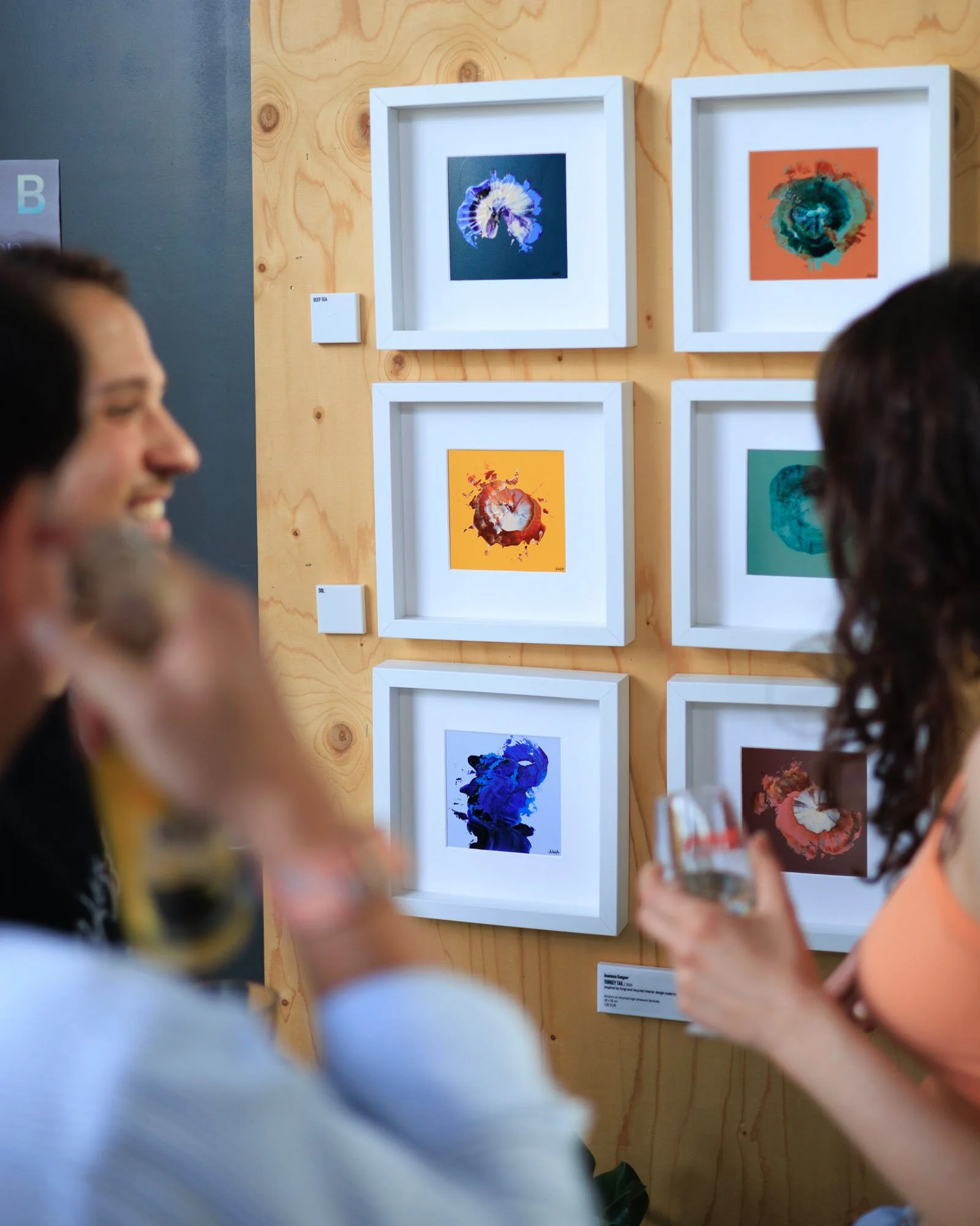 People viewing abstract watercolor paintings in a gallery, with some smiling and taking photos.