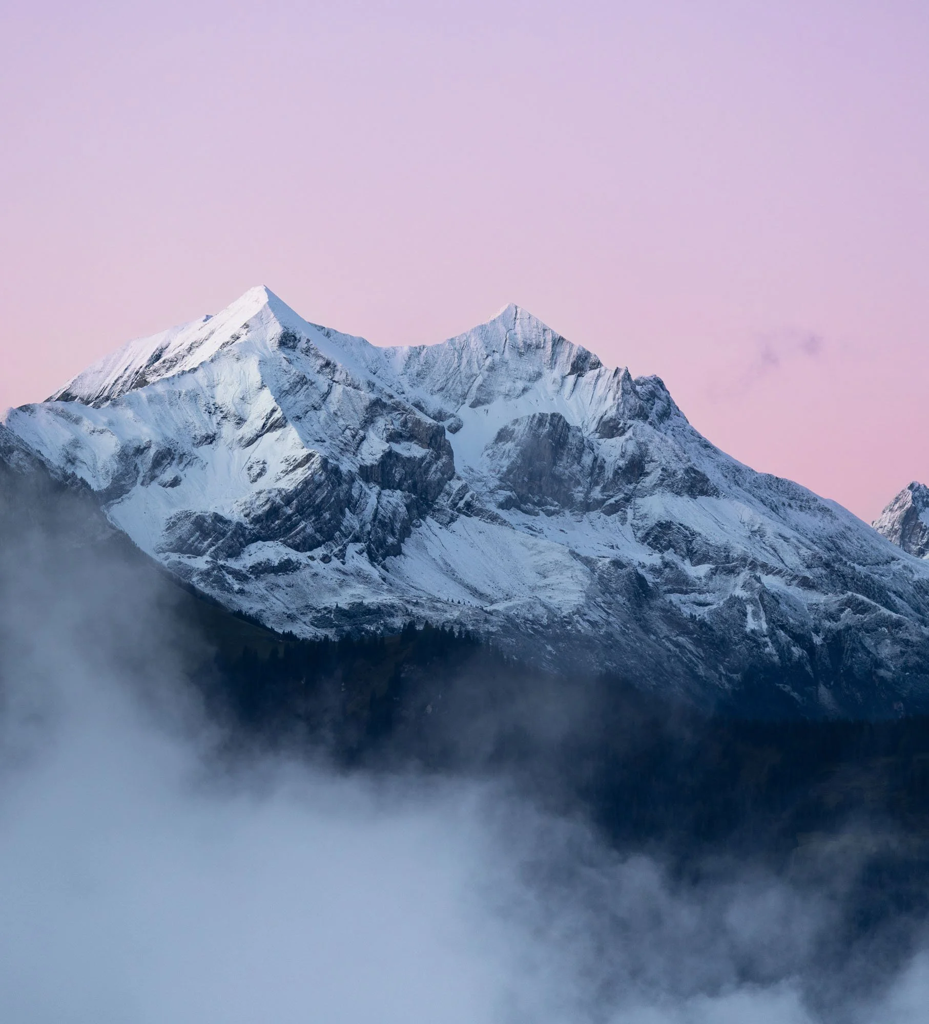 Snow-covered mountain peaks under a pink and purple sky.