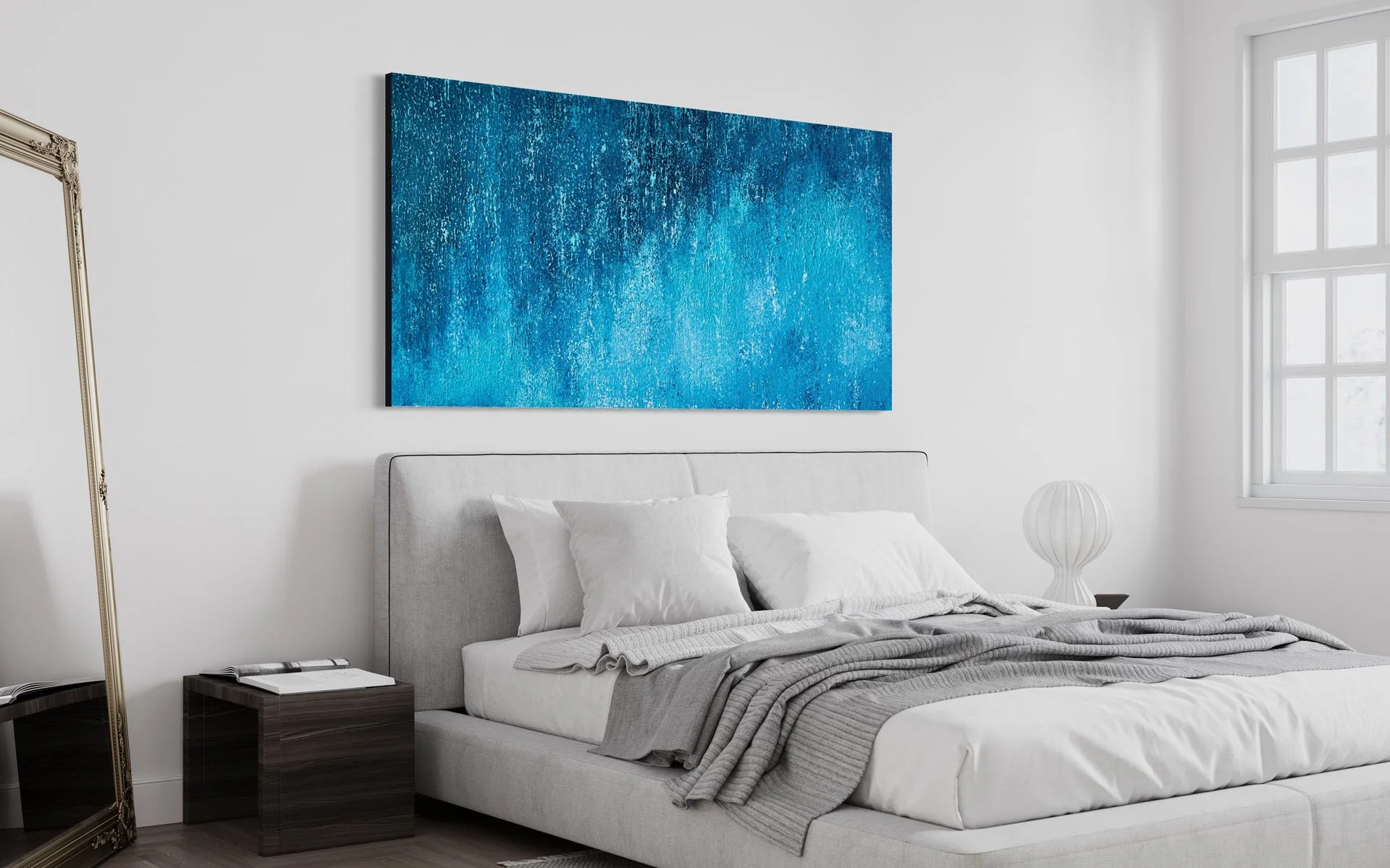 Modern bedroom with a large abstract blue painting above the bed, white walls, a gray upholstered bed with white pillows, a dark wood nightstand, and a spherical table lamp. A large window lets in natural light.