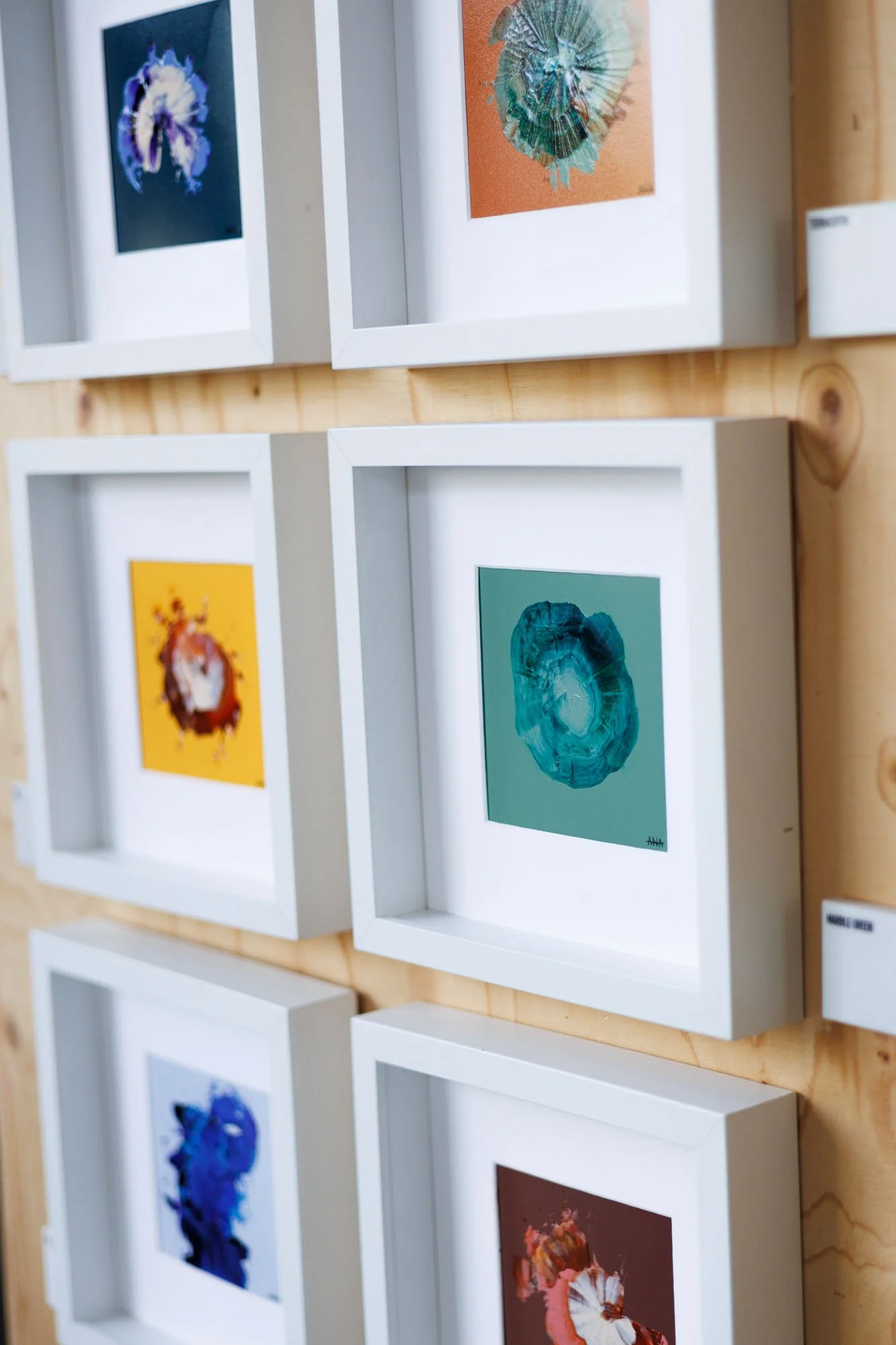 Gallery wall with framed abstract artwork of various colors and textures on a wooden wall.