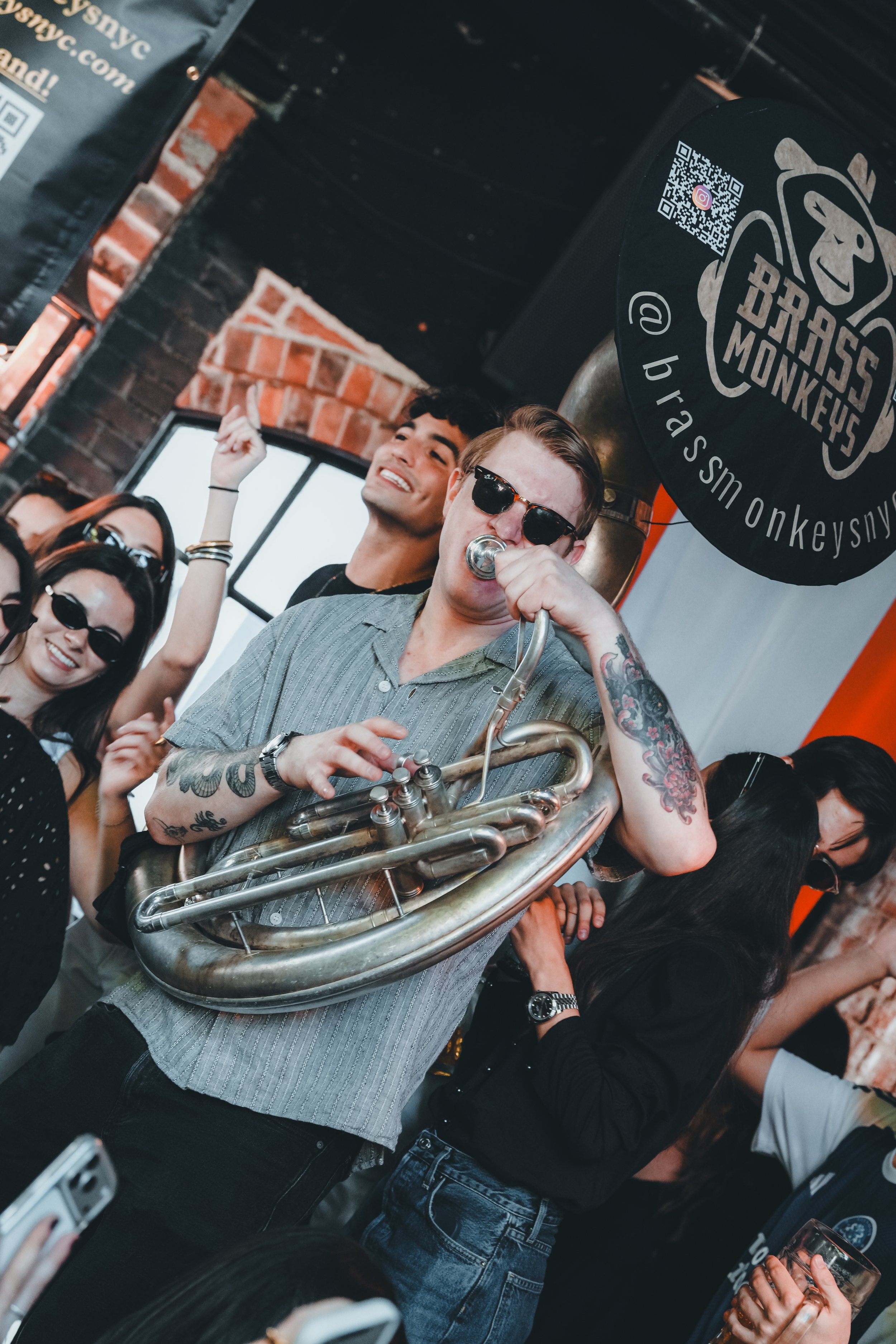 A man playing a trumpet in a lively, possibly indoor setting with wooden and brick walls, and warm lighting.