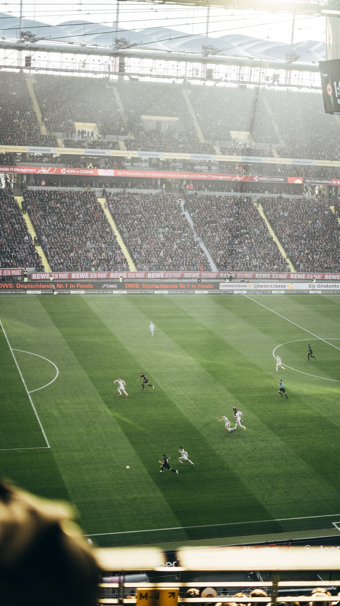 View of a soccer stadium with players on the field and a large crowd of spectators in the stands.