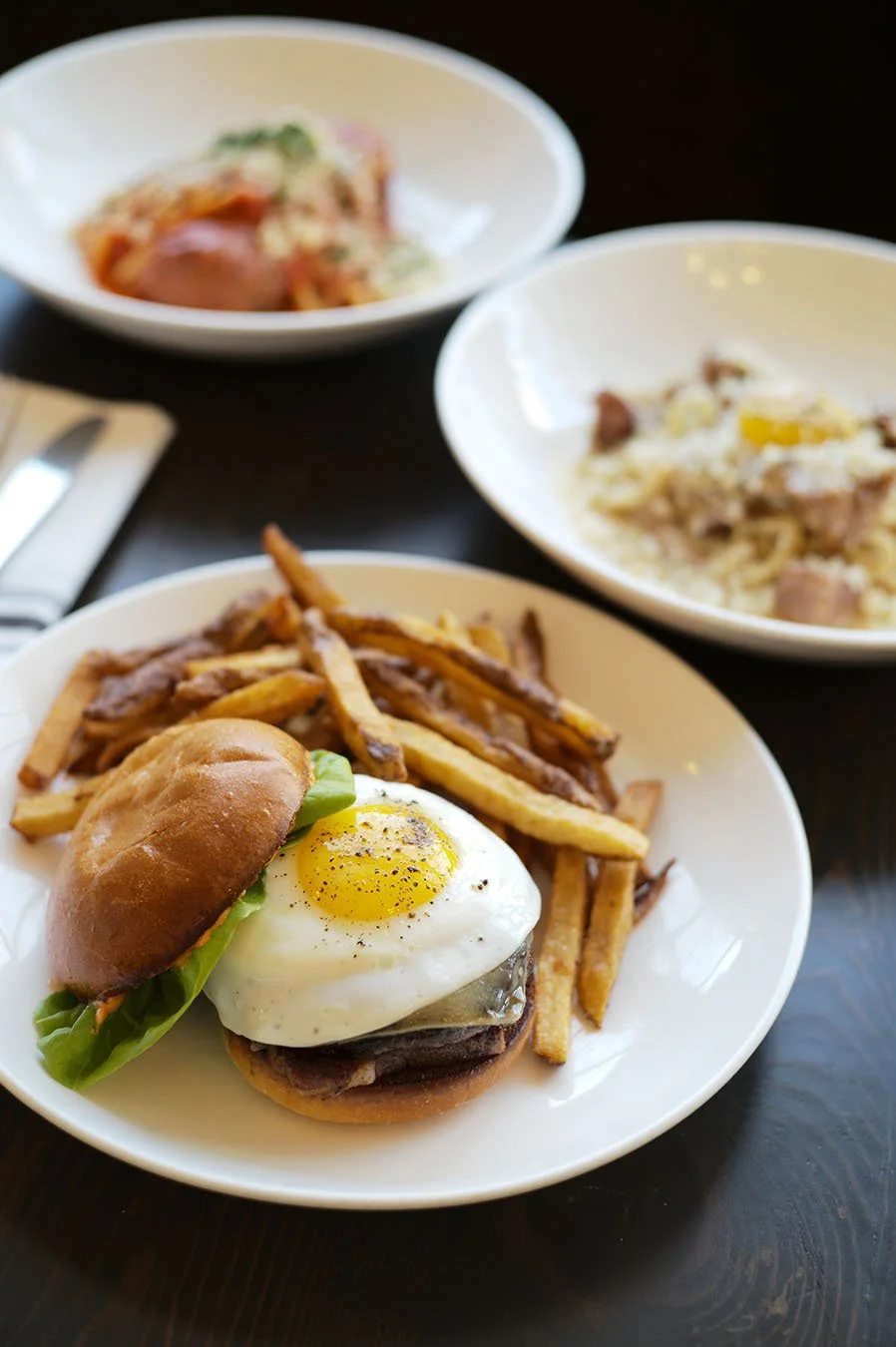 The Kenwood burger with sakura farms wagyu beef and a fried egg on a brioche bun, with homemade pasta dishes in the background.
