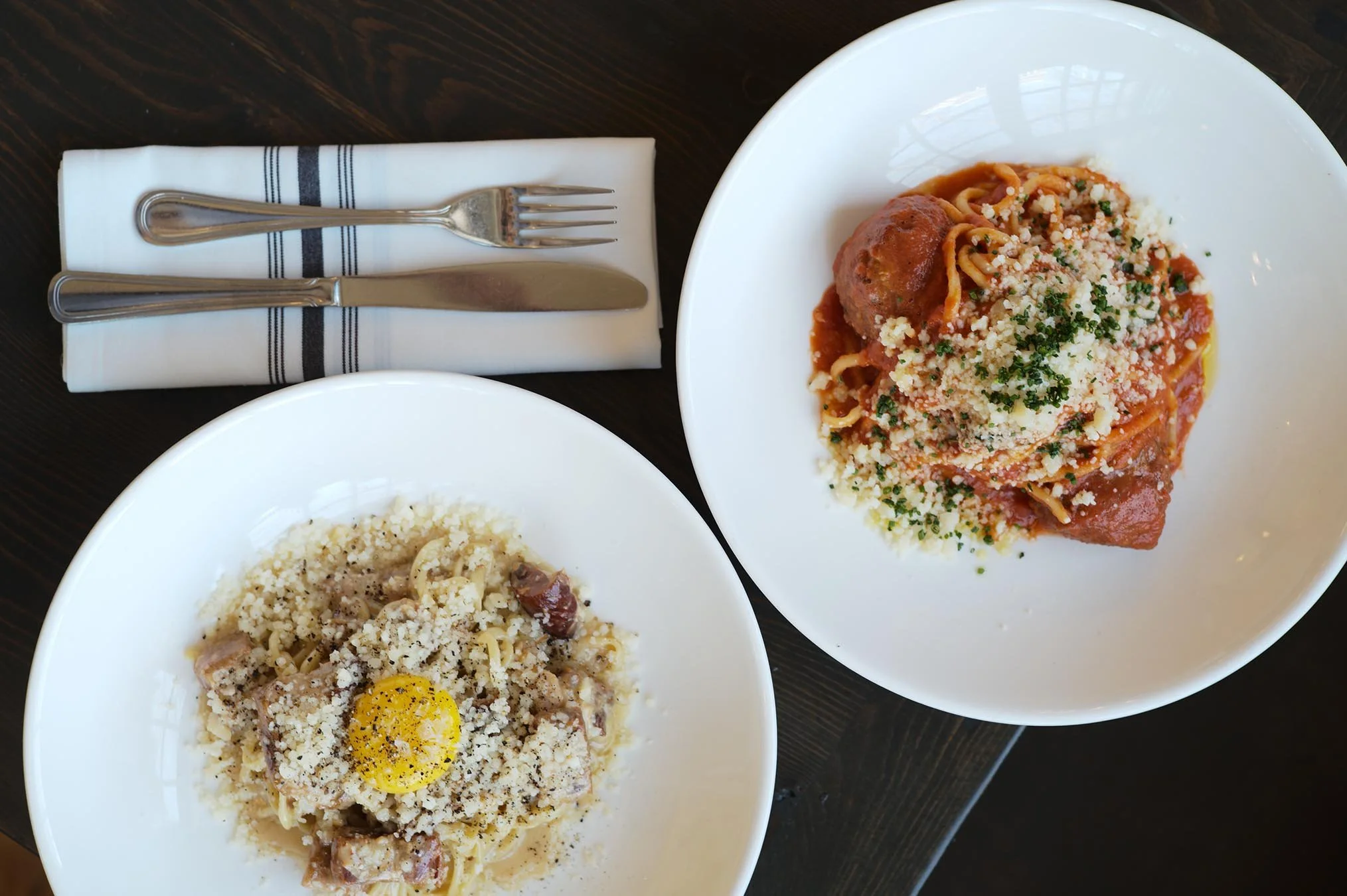Two beautifully plated homemade pasta dishes including bucatini carbonara and spaghetti with meatballs.