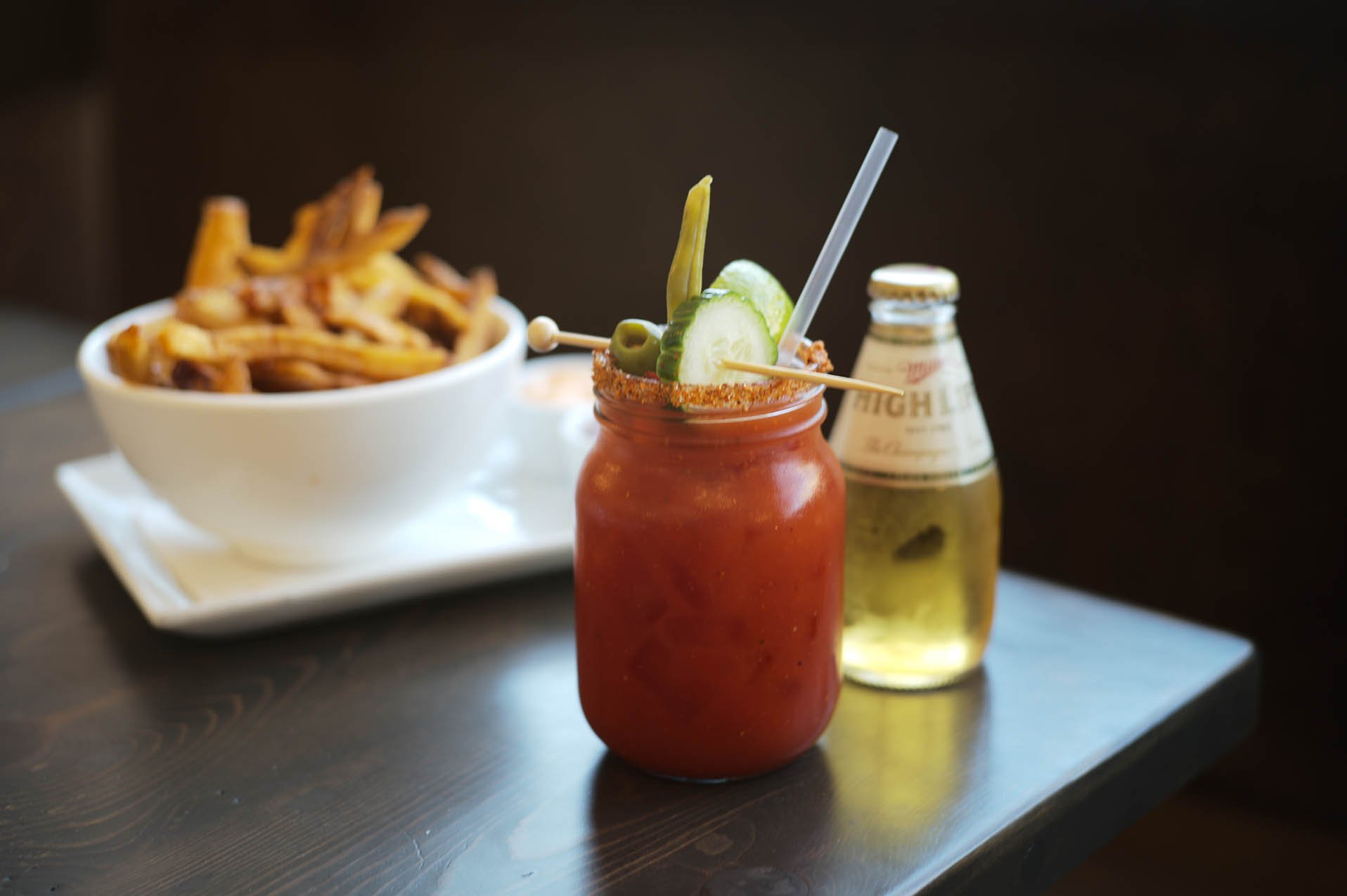 Bloody mary in a mason jar with pickled vegetables, and beer and french friends in the background.