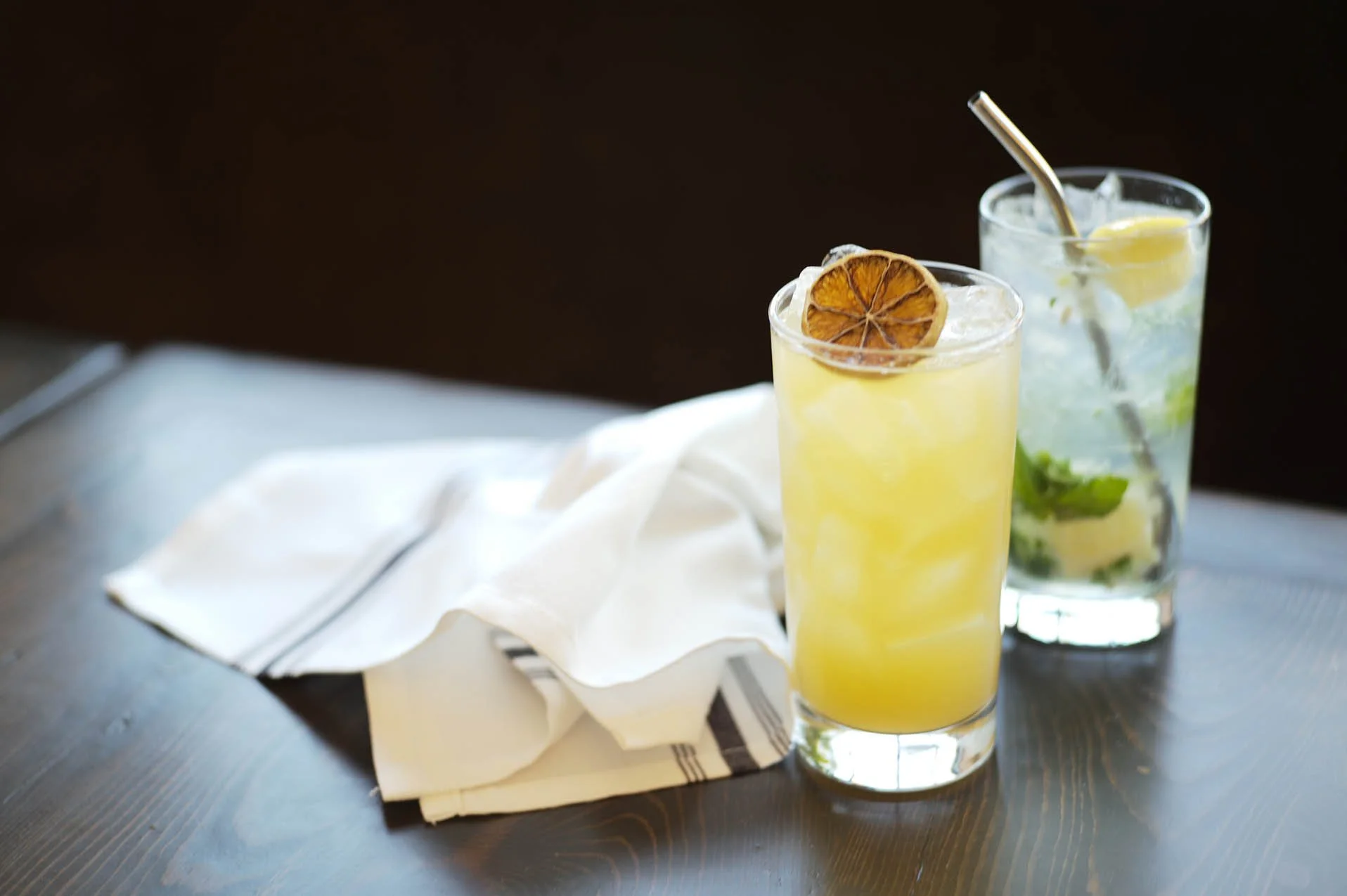 Pair of drinks in collins glasses with dried citrus garnish.