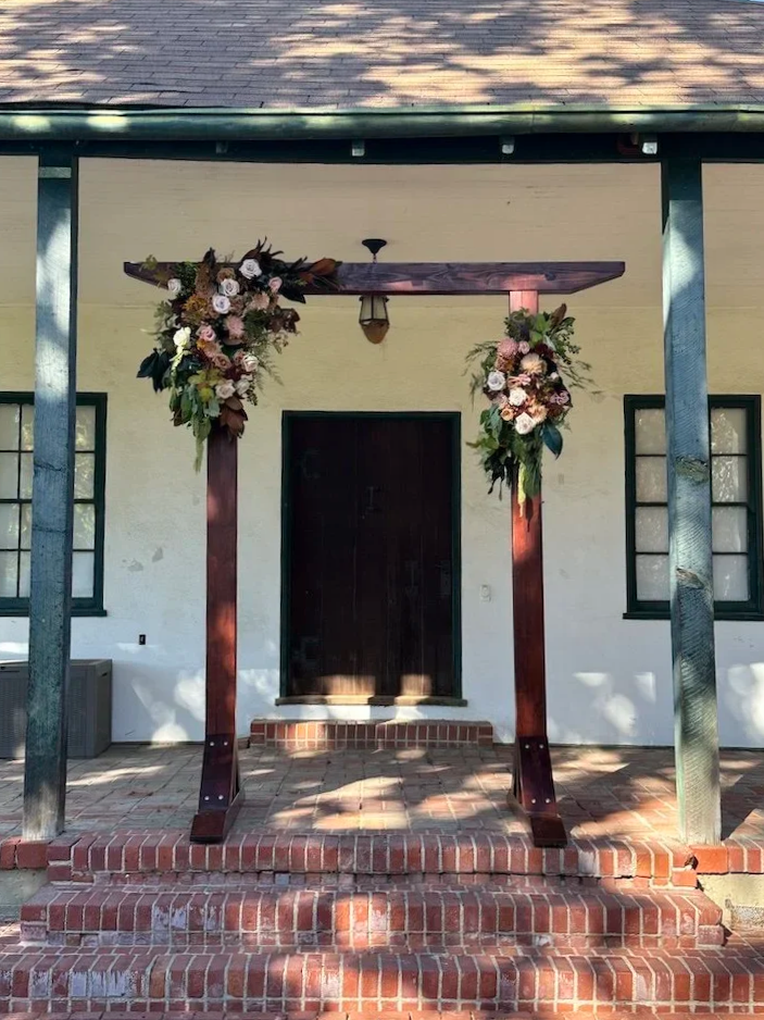 Wedding arch decorated with flowers on a brick porch in front of a house.