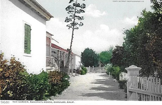 Street scene in Camulos, California with white houses, a dirt road, trees, and shrubs.