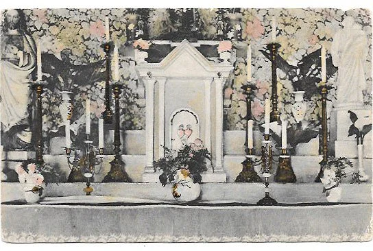 An altar with seven candles, two vases with flowers, and a framed picture, set against a backdrop of decorated wall with floral patterns.