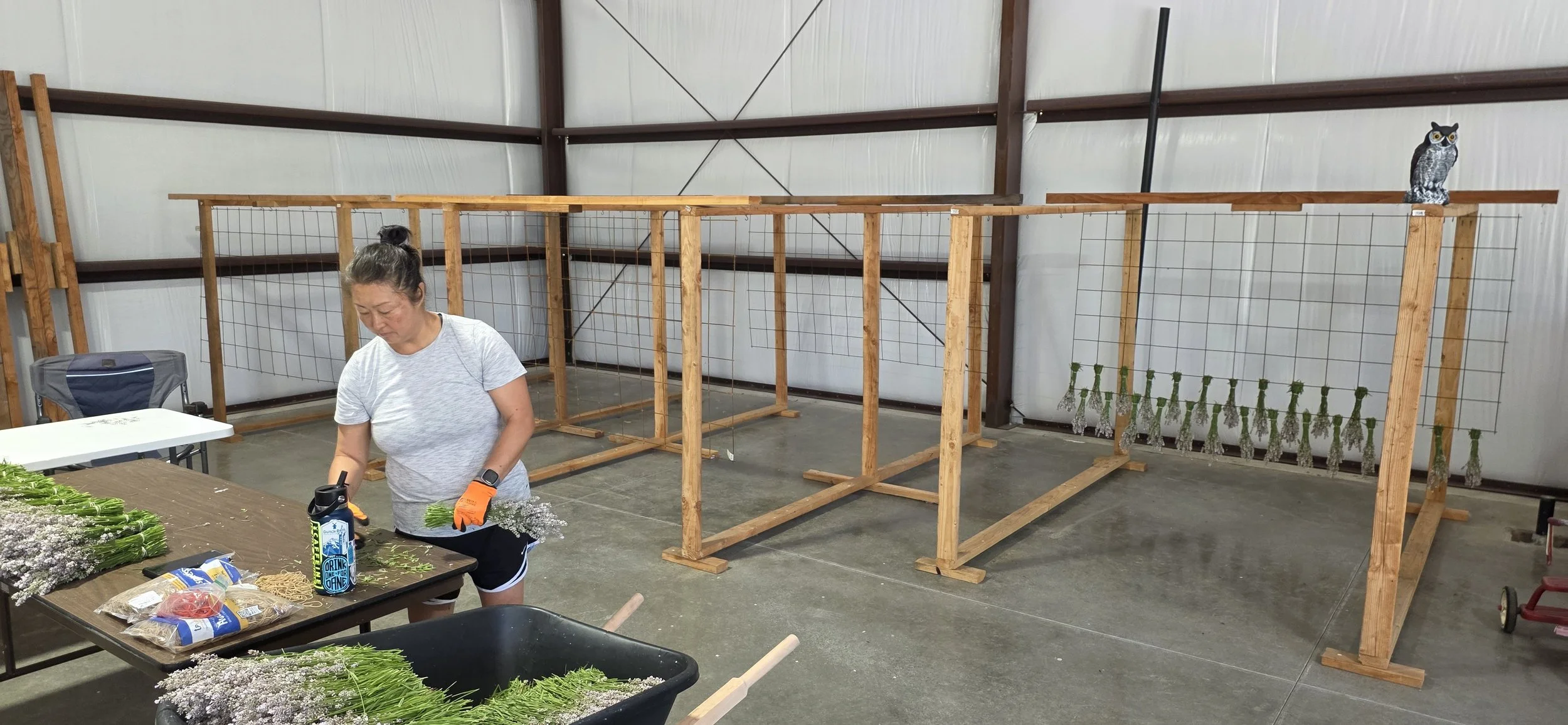 Woman preparing flowers at a table inside a warehouse with wooden plant display stands and owl decorations on the stands.