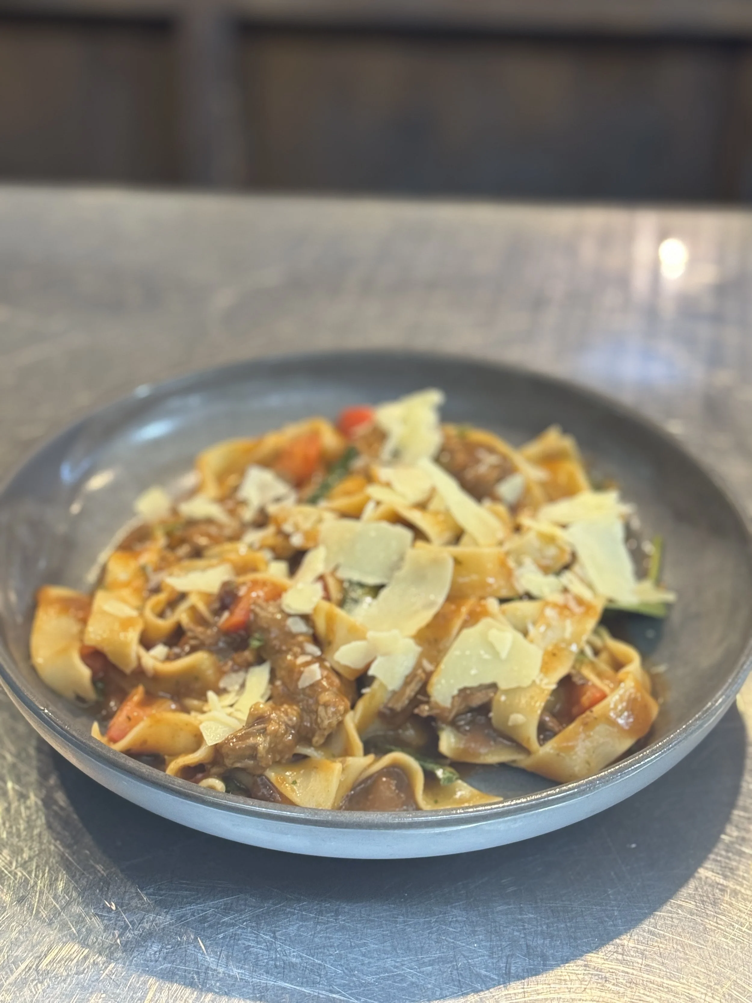 Plate of beef and vegetable pasta topped with shaved cheese.