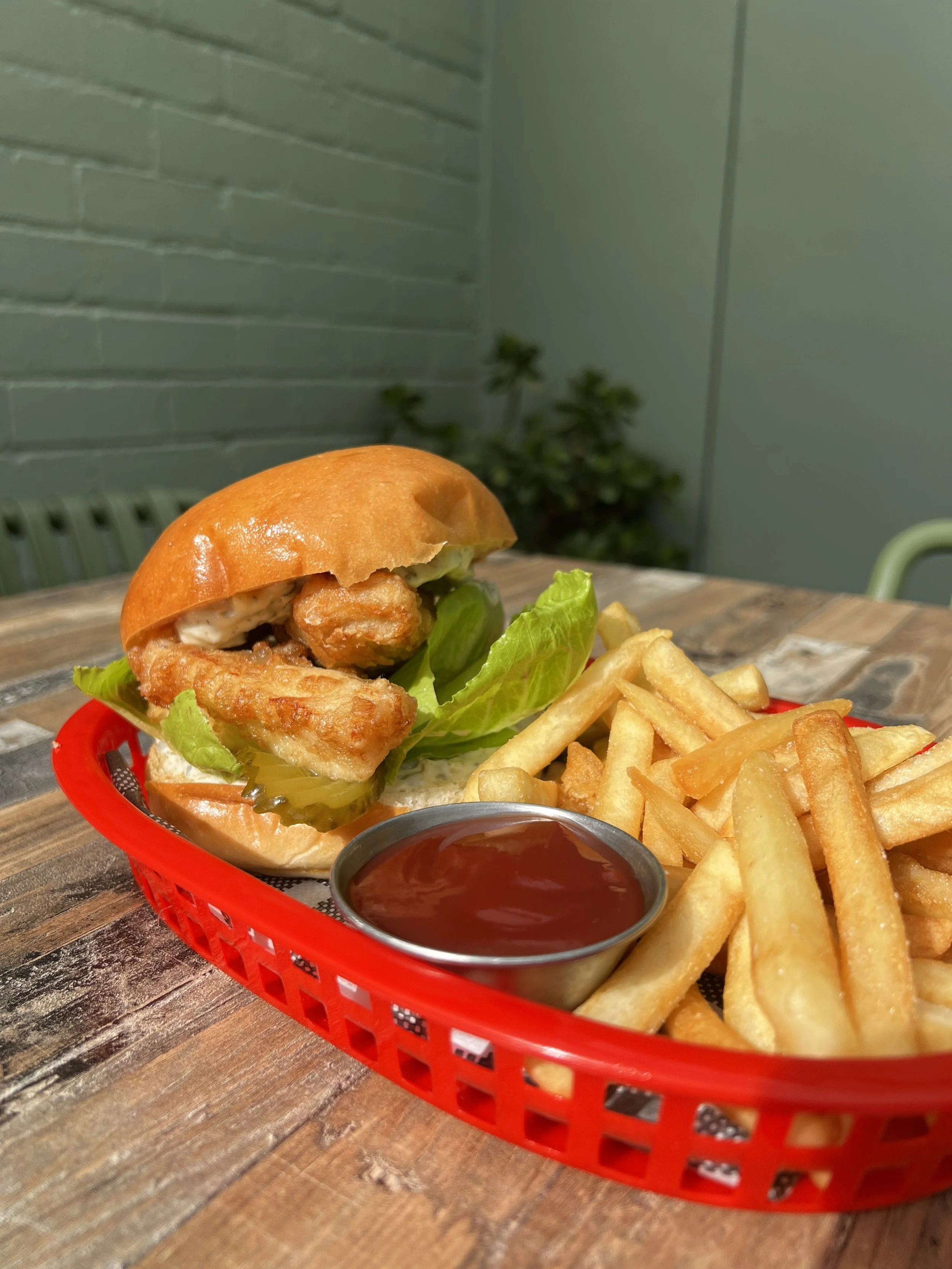 A tray of fast food with a cheeseburger with lettuce, fried chicken, French fries, and a cup of ketchup on a wooden table.