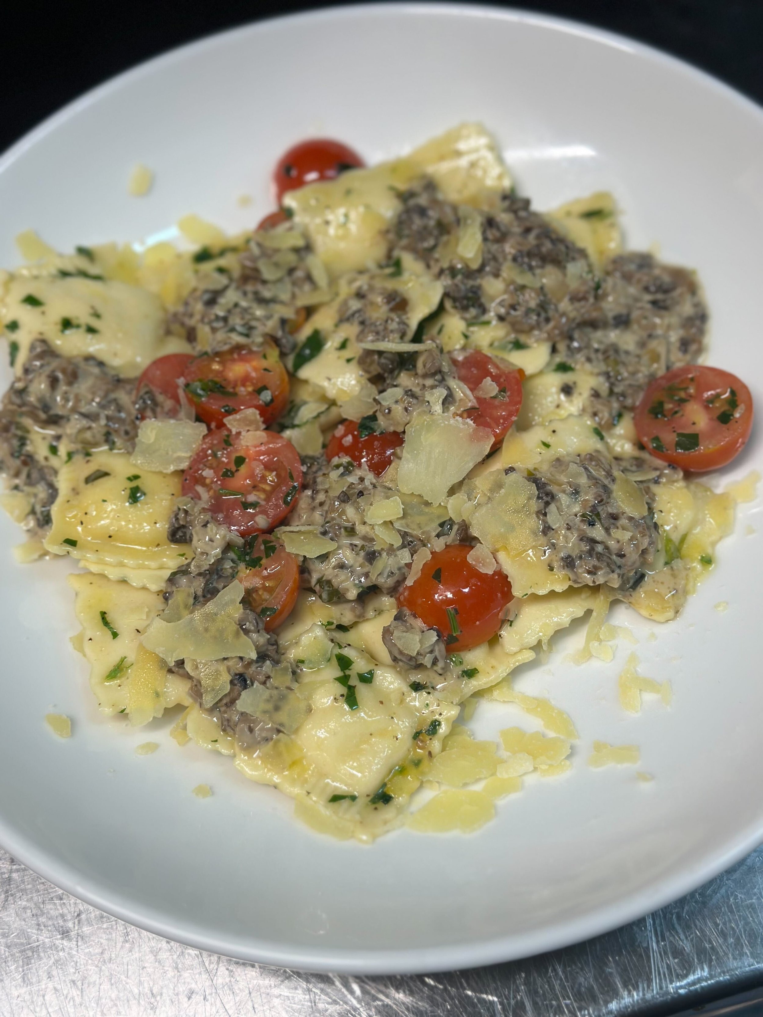 Plate of ravioli pasta with cherry tomatoes, chopped herbs, and a creamy mushroom or truffle sauce