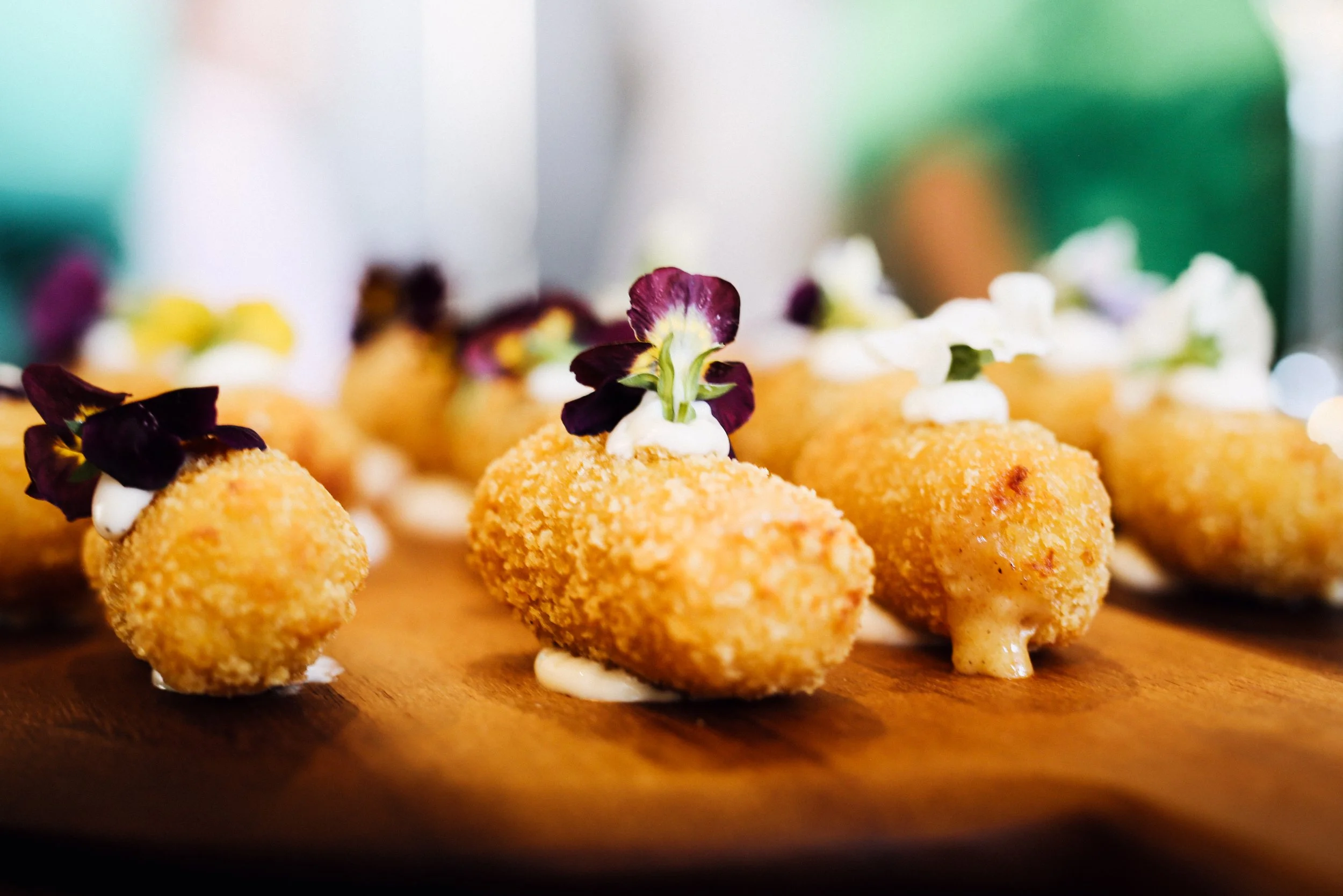 Fried food bites garnished with edible flowers and cream on a wooden board.
