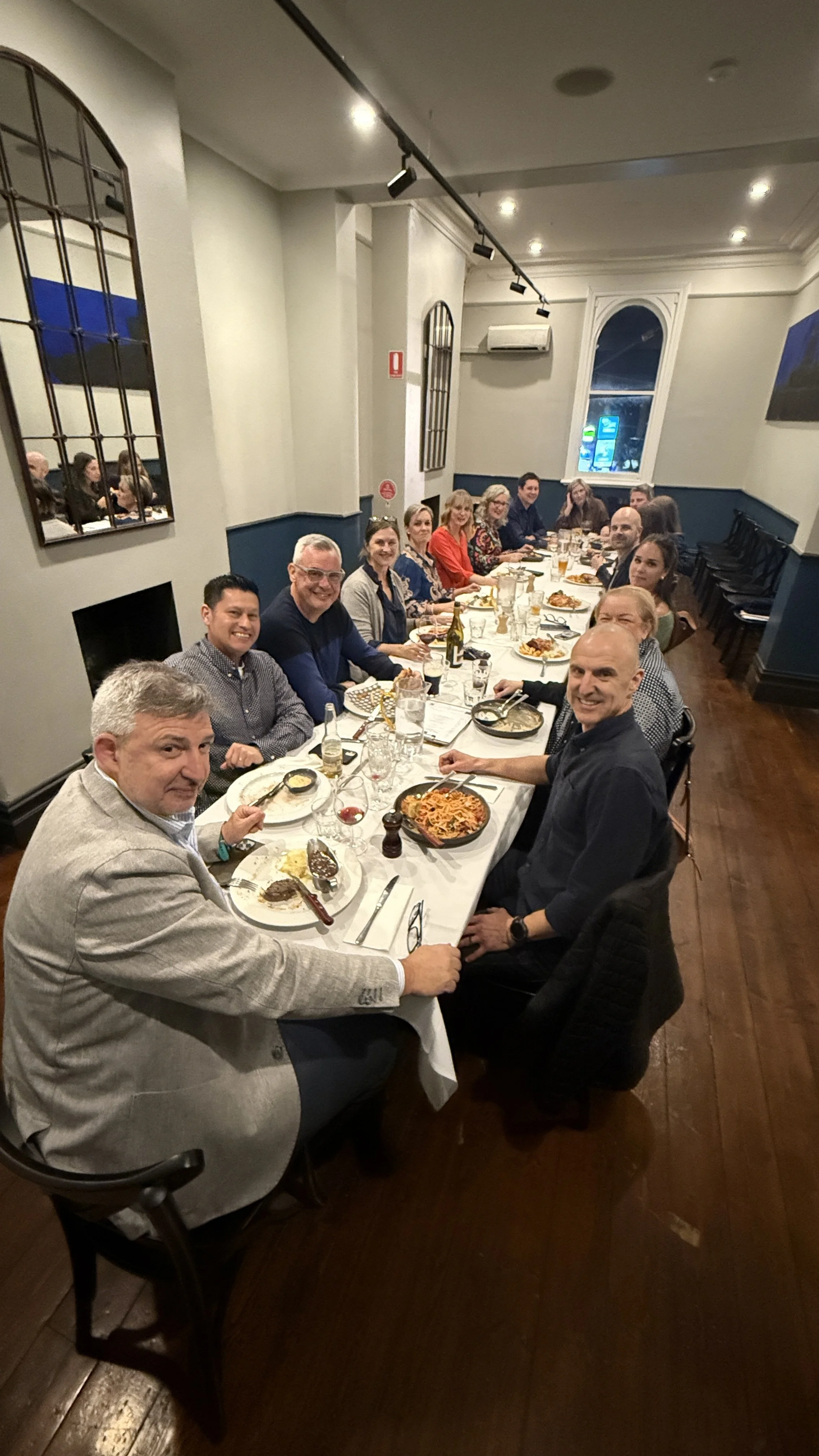 People enjoying a celbration dinner on a long table with white table clothers, two lit fireplaces in the Palace Hotel Long Room - upstairs at the Palace