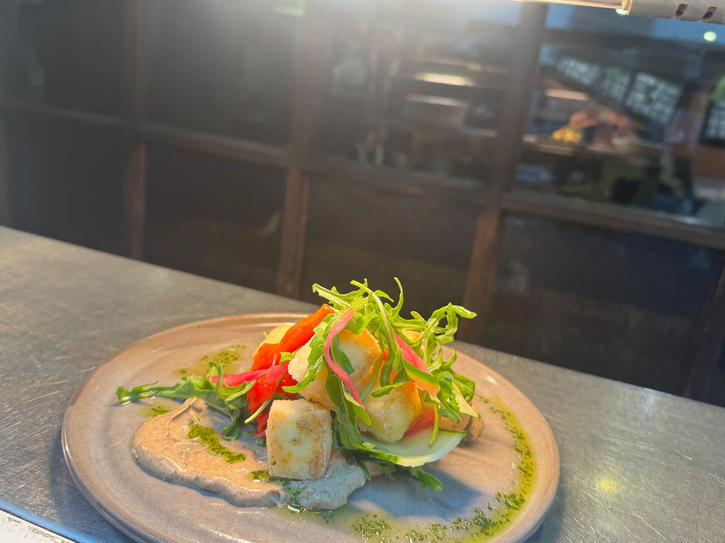 A colorful salad with leafy greens, vegetables, and croutons served on a plate, with a kitchen reflecting in the background.