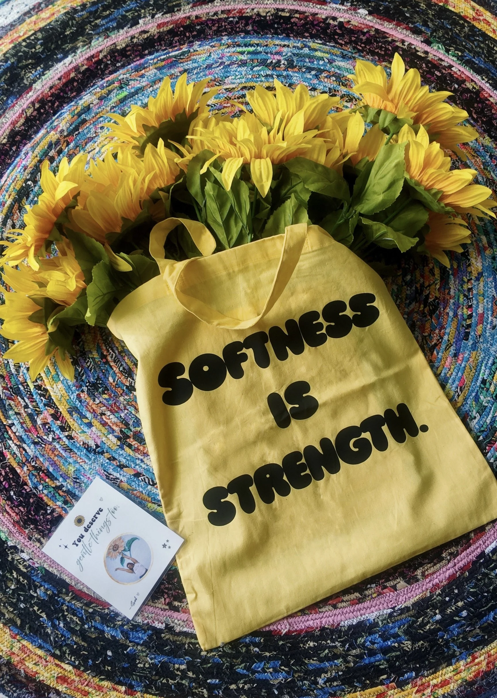 Yellow Softness Is Strength cotton tote bag displayed on colorful handmade rug
