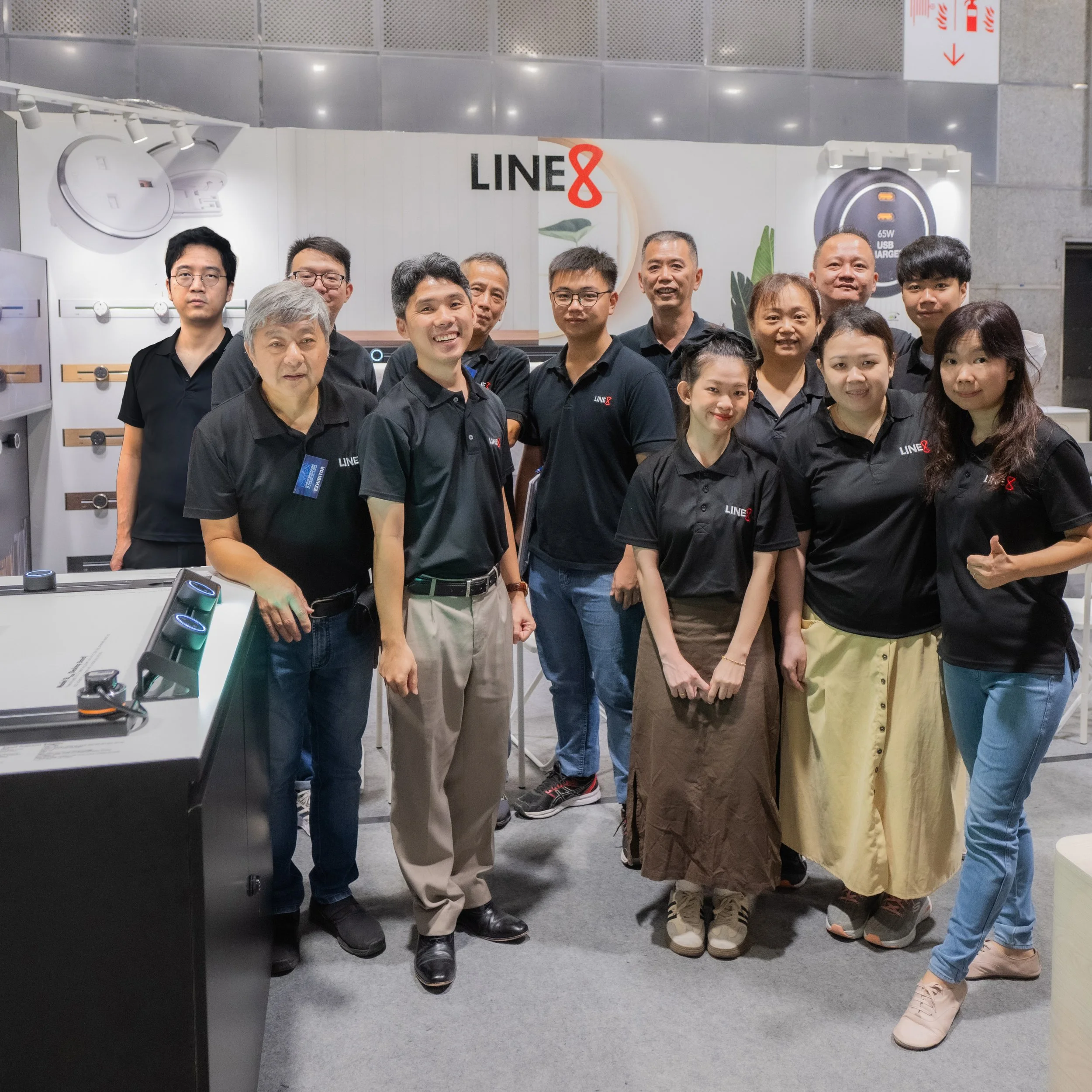 The Line8 sales team standing together at a technology booth with a sign that says 'LINE8' in the background, displaying various tech gadgets including watches and chargers.