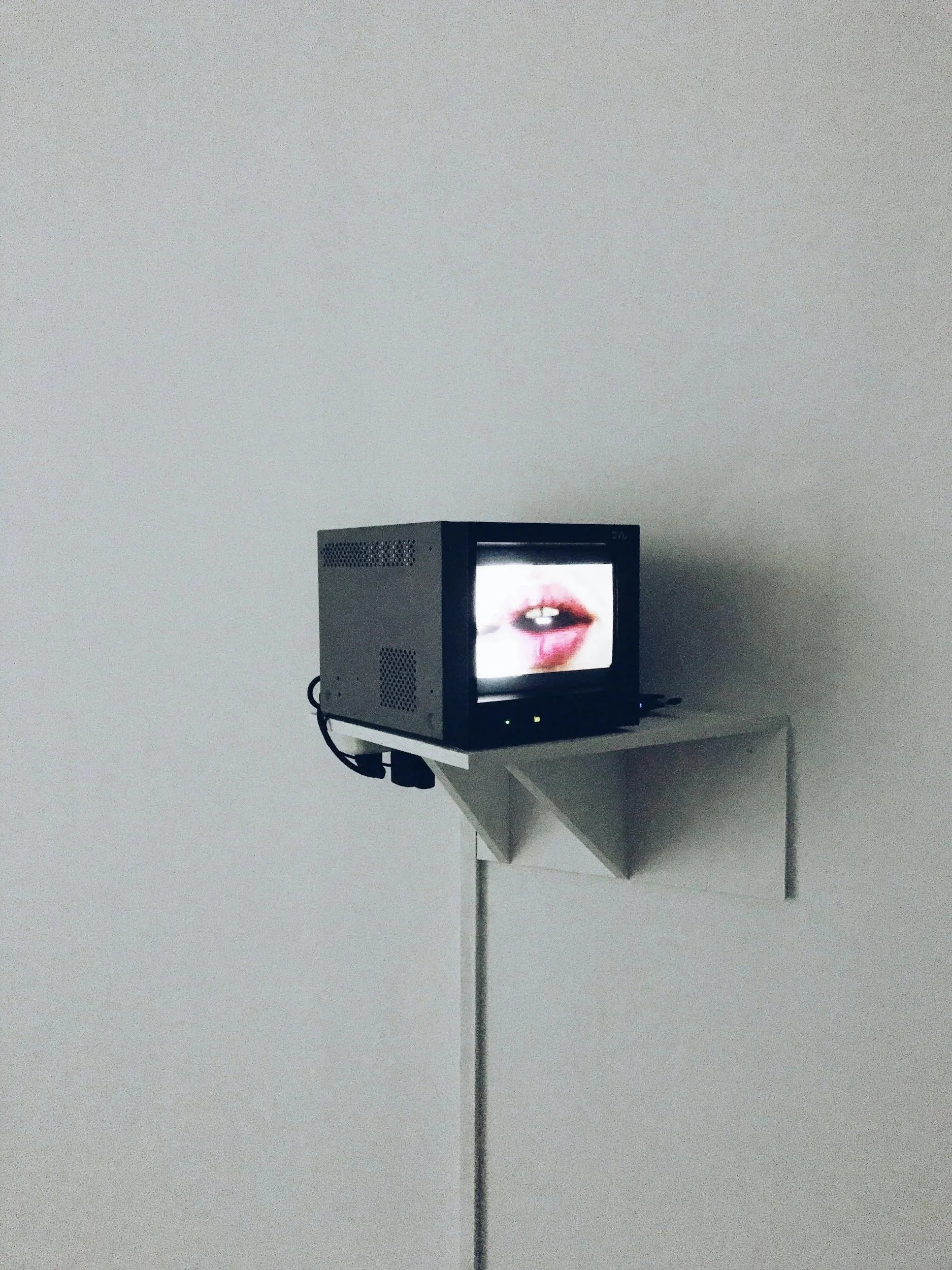 A small CRT television on a wall-mounted shelf displaying a close-up of a person's lips and teeth.