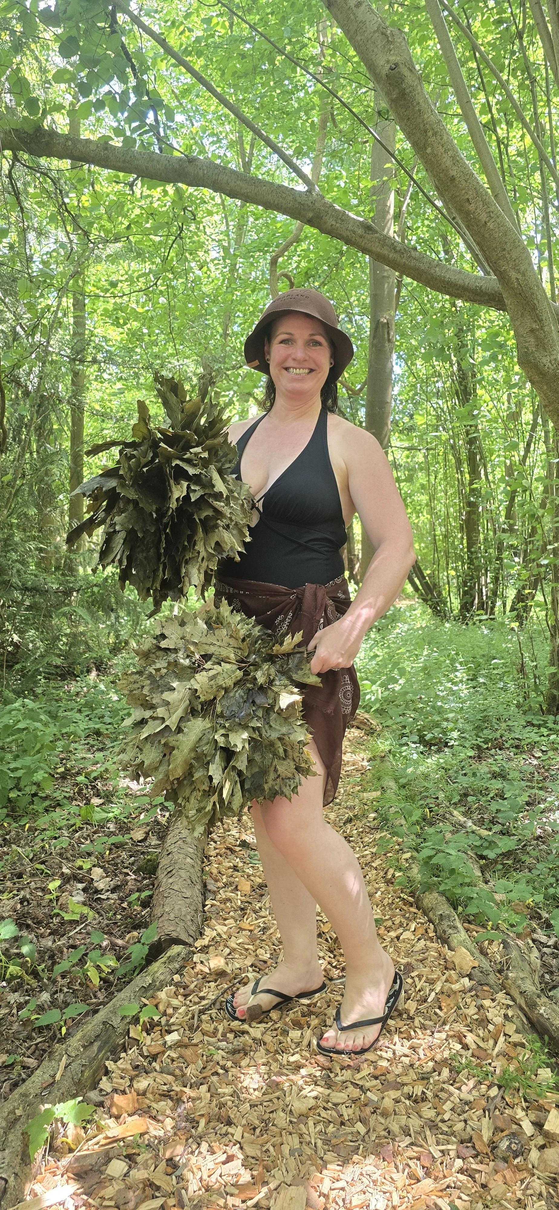 Sauna Master Chantelle in woodland, holding 2 oak whisks