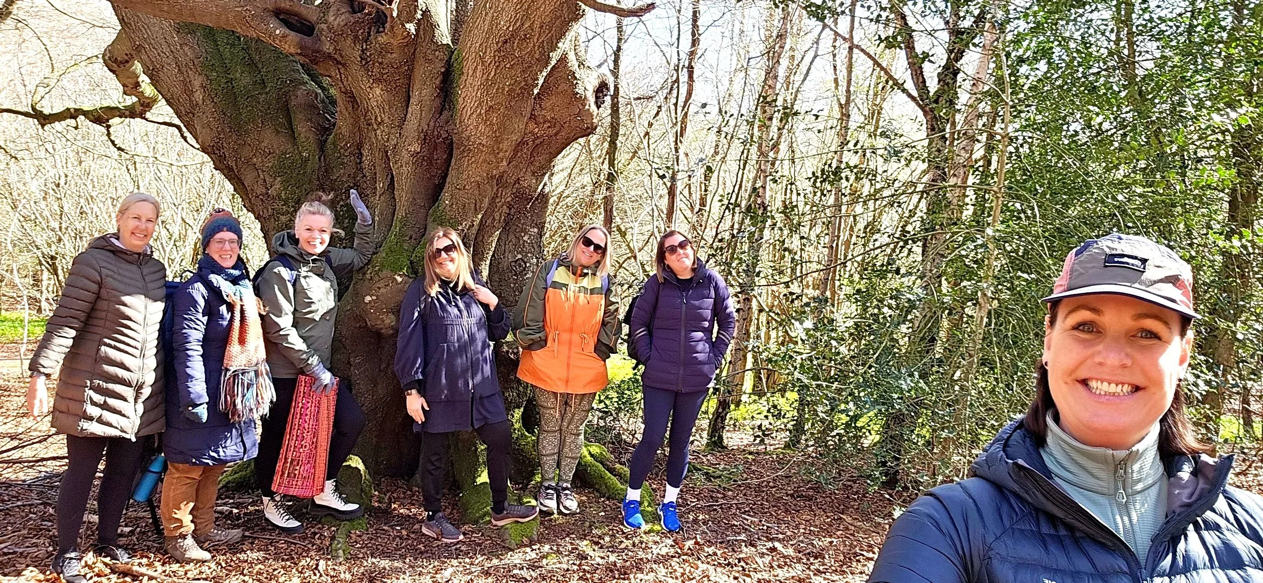 Chantelle the forest bathing guide smiling with a group of women in the background smiling next to a large tree trunk