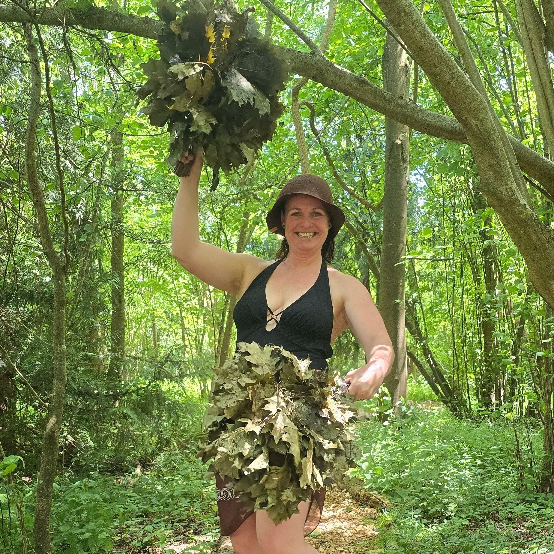 Sauna Master Chantelle holding up her oak whisks in a woodland setting