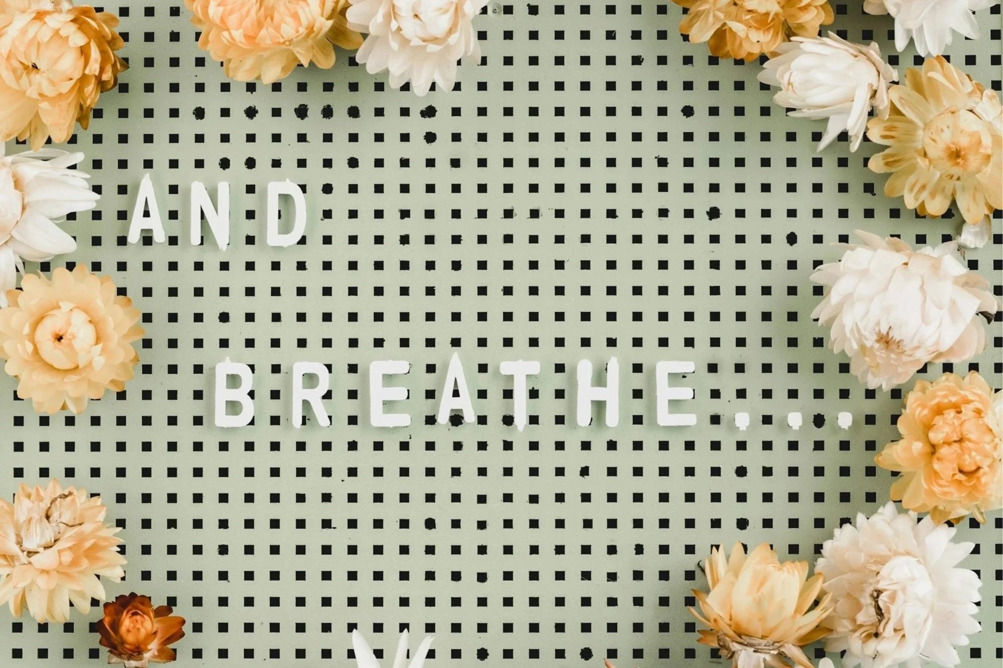 Letterboard with the words 'AND BREATHE' surrounded by white and peach flowers.