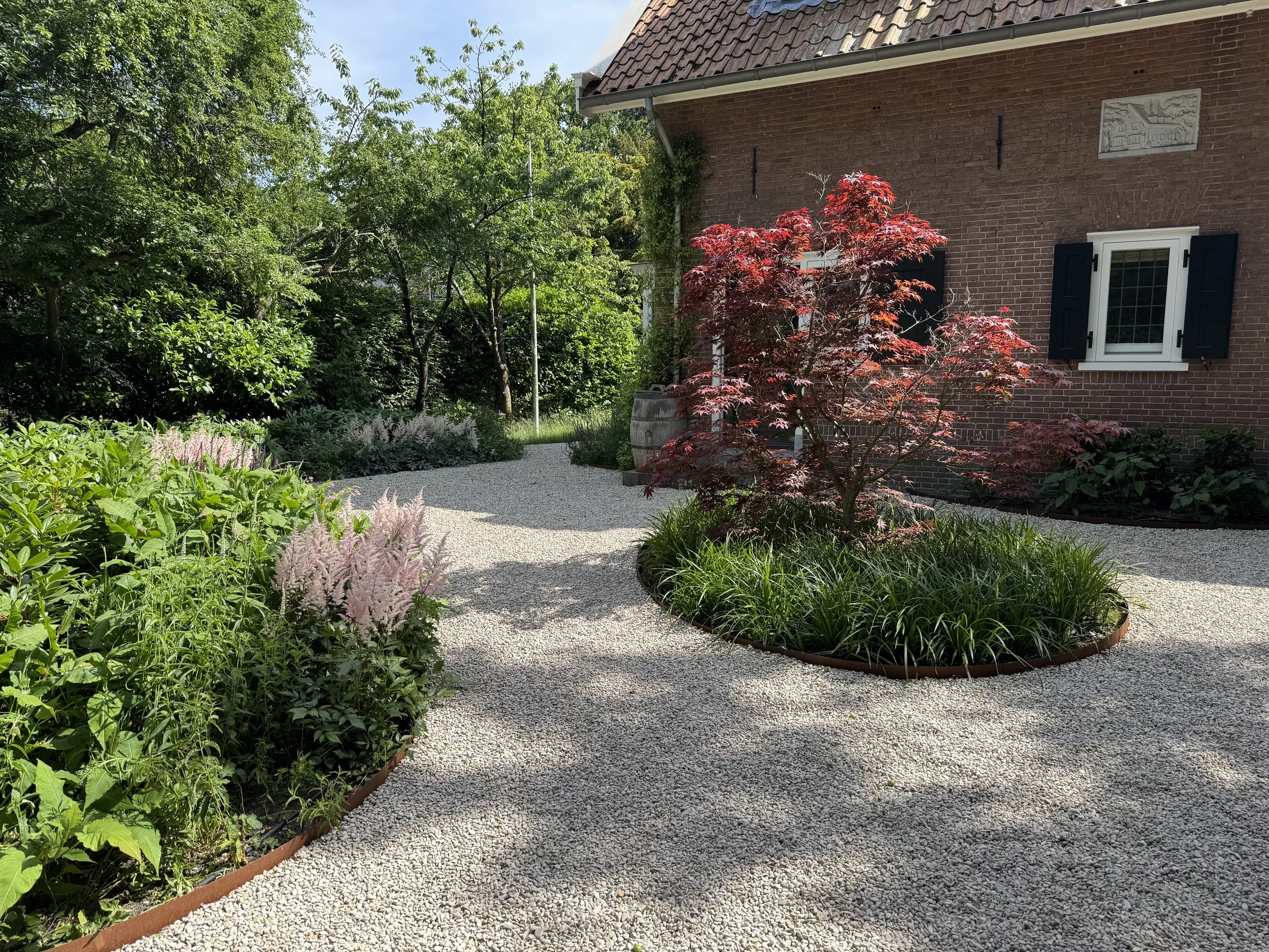 Gerealiseerde tuin met grindpaden en weelderige beplanting bij een bakstenen woning.