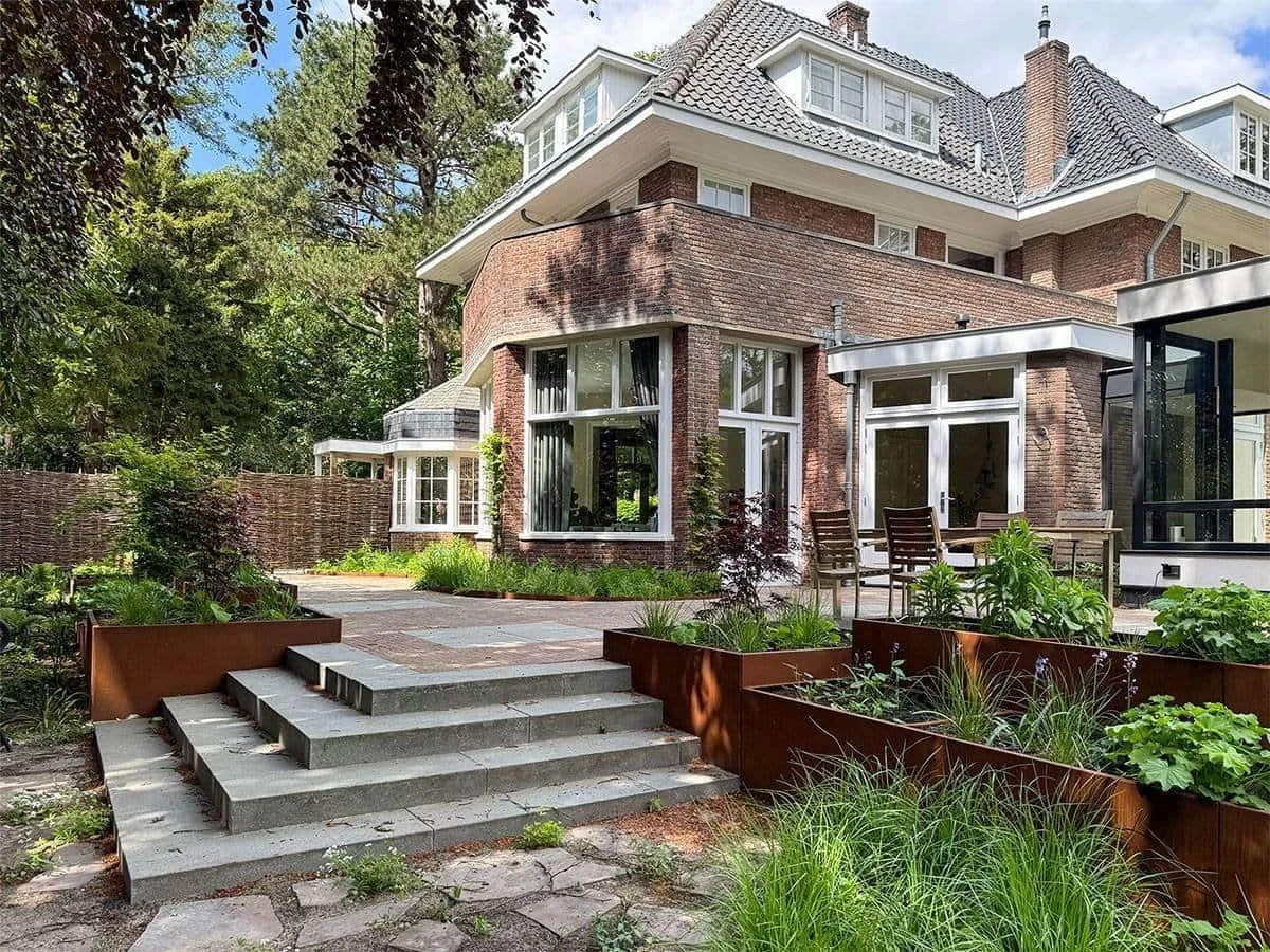 Klassieke bakstenen villa met een exclusief tuinontwerp, voorzien van stenen trappen en cortenstalen borders.