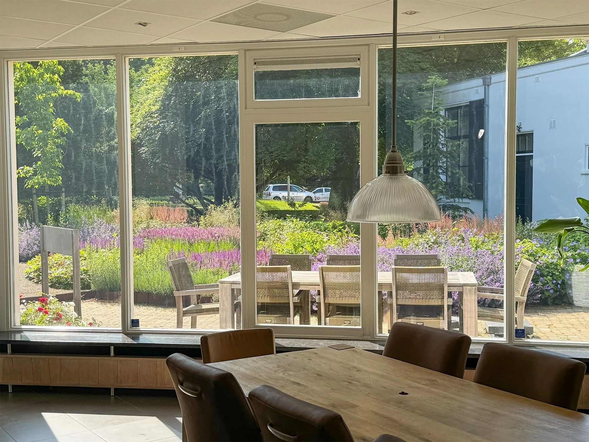 Vanuit de overlegruimte biedt de raampartij direct zicht op de weelderige kantoortuin. Het ontwerp integreert de functionele werkplek visueel met de natuurlijke buitenruimte, wat zorgt voor een rustgevende werkomgeving.