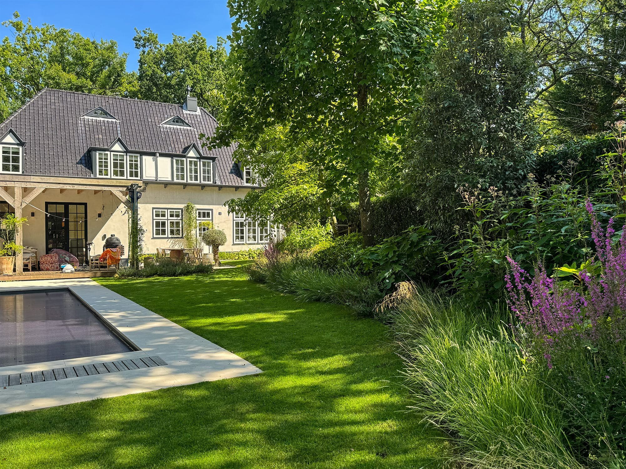 De strakke lijnen van de lichte zwembadrand vormen een architectonisch contrast met het organische karakter van het omringende bos. Volwassen bomen bieden natuurlijke schaduw en waarborgen de privacy rondom de villa.