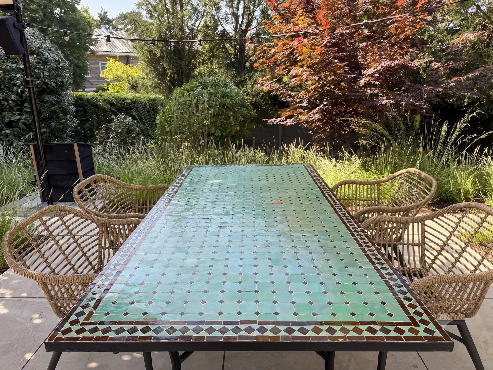 Het ruime, verhoogde terras is ontworpen als een centraal leefgebied. Door het strategische hoogteverschil ontstaat er een geborgen zithoek rondom de grote mozaïektafel, die optisch volledig wordt omarmd door de omringende plantenborders.