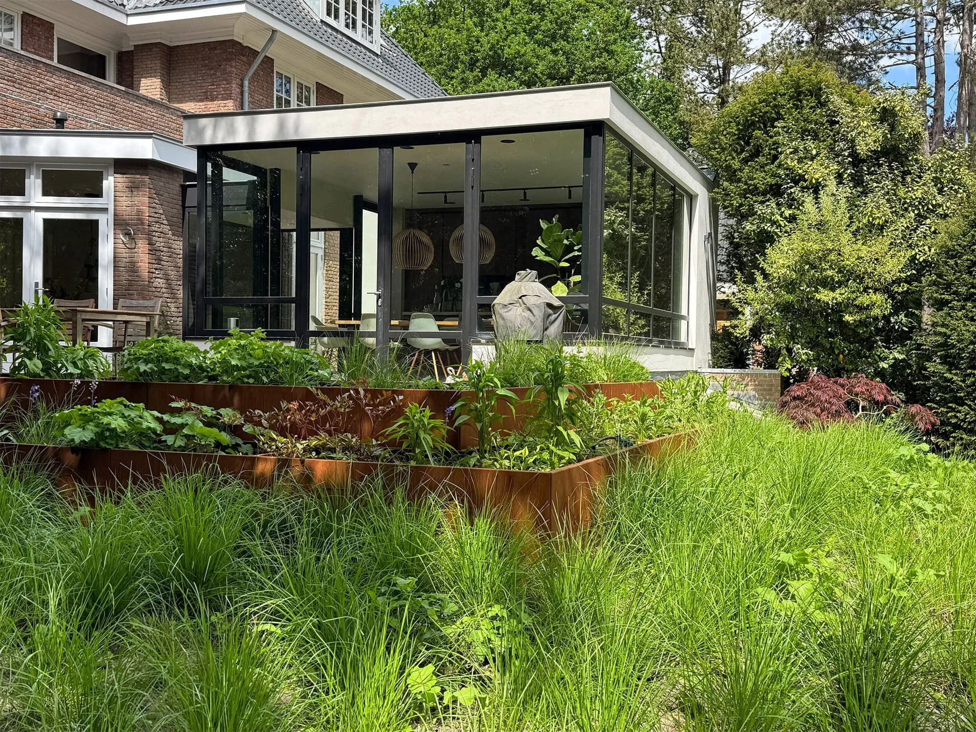 Bakstenen villa met moderne glazen aanbouw en een weelderige tuin met cortenstalen plantenbakken.