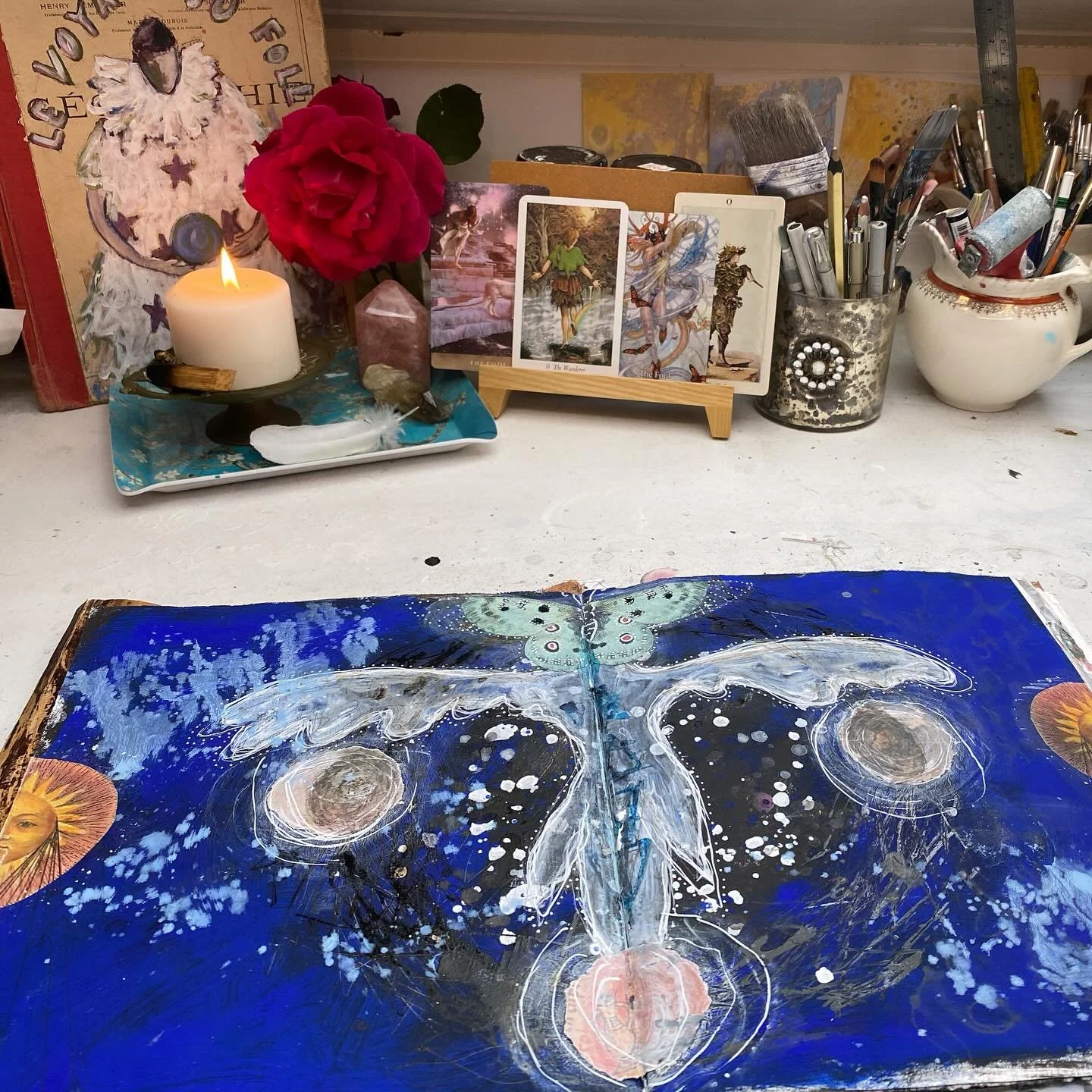 Art journal spread of the Fool archetype, open on a desk with tarot cards, candles and art supplies