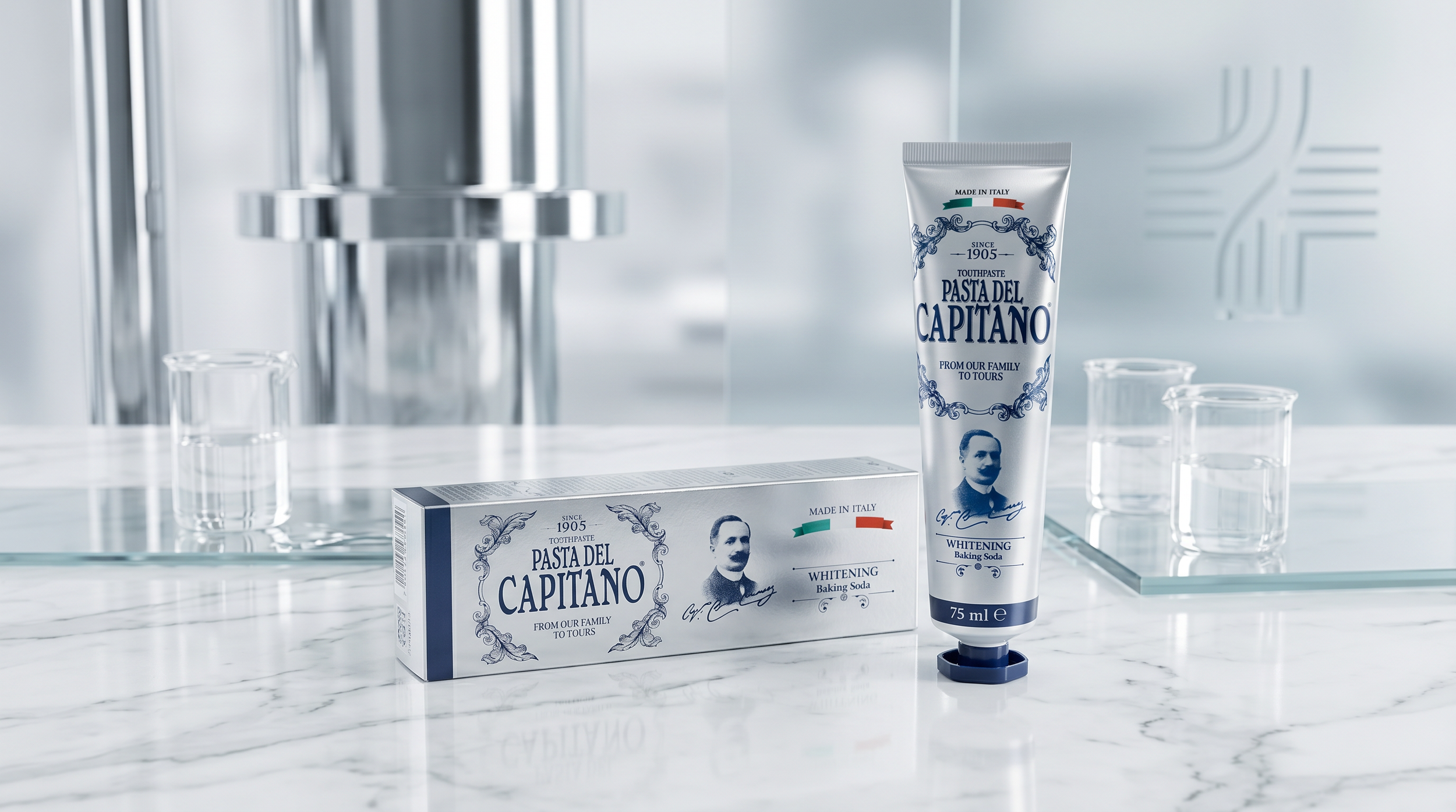 A tube of Pasta del Capitano whitening baking soda toothpaste and a matching box on a marble countertop, with four empty glass beakers and a metallic wall in the background.