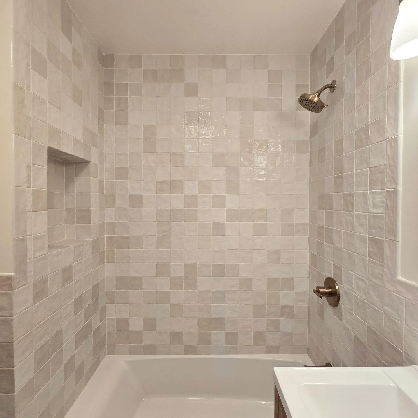 For this renovation, the goal was to maximize light and texture without changing the footprint. We used Zellige-style square tiles to bounce light around the room, added a custom built-in niche for a clean look, and brought in natural wood and brass 