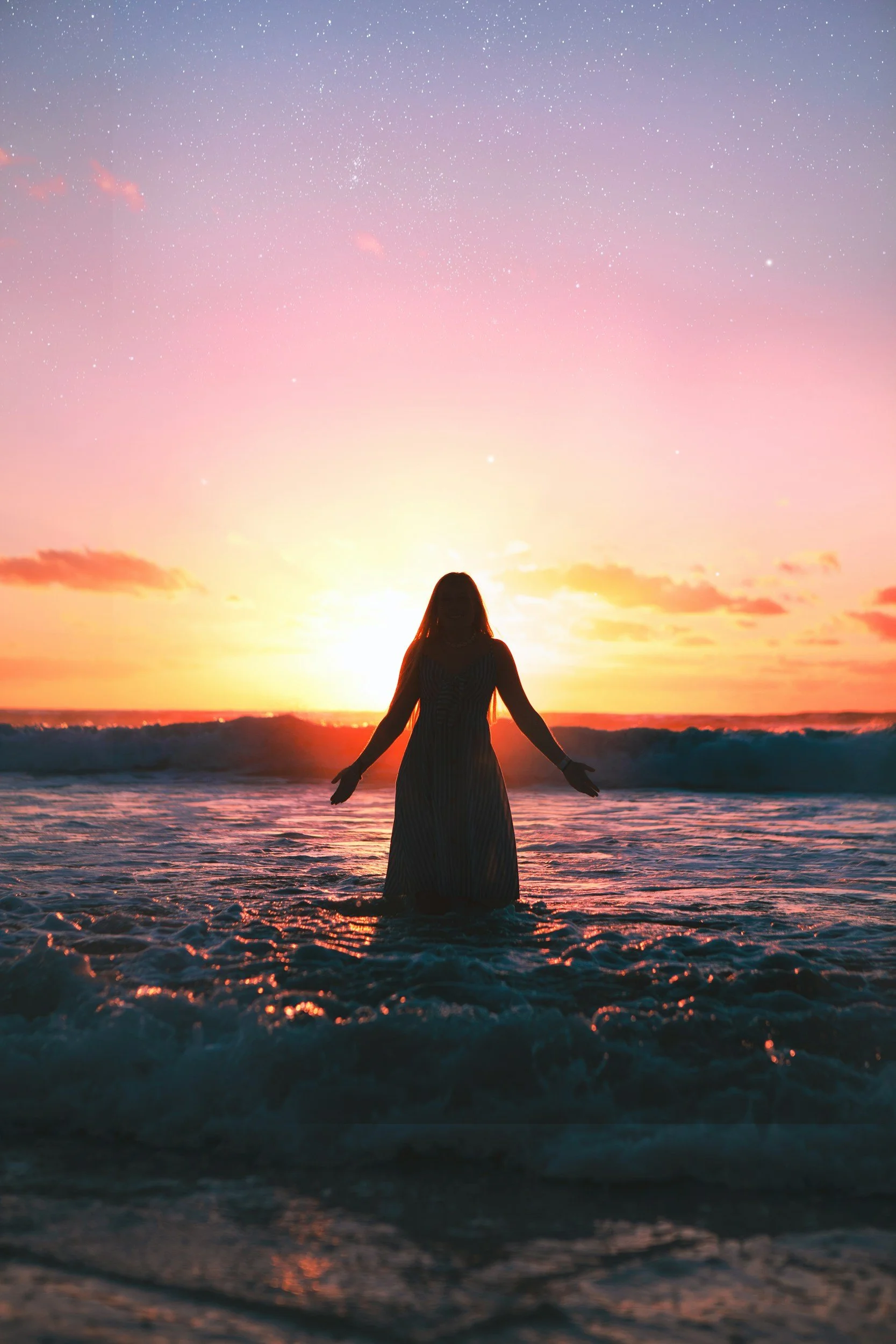 Silhouette of a woman standing in the ocean during sunset with a colorful sky.