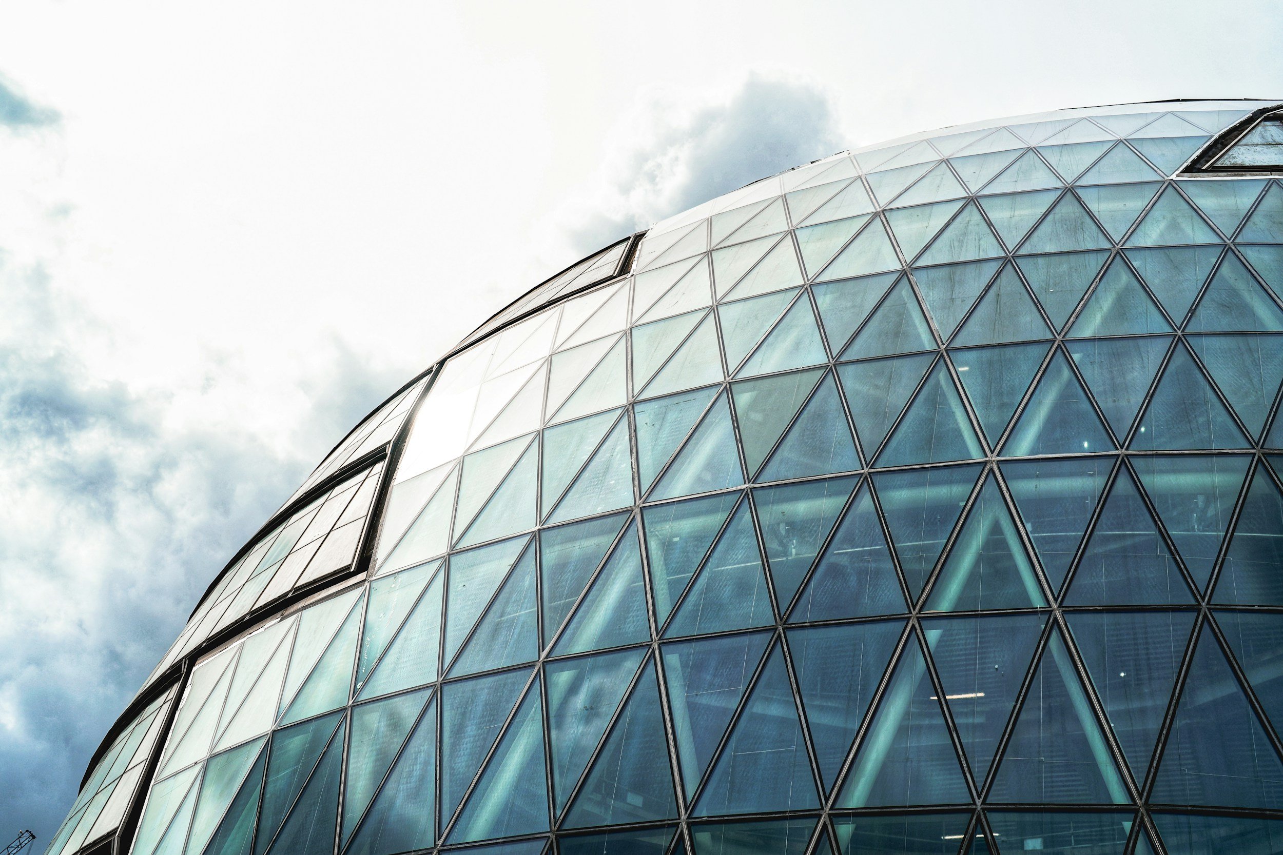 Moderni lasikuoriomainen rakennus, jonka pintaa peittää geometrinen metallirakenne ja lasipintoja, sekä osia, joissa ikkunat ja teräsvälit näkyvät. Taustalla pilvinen taivas.