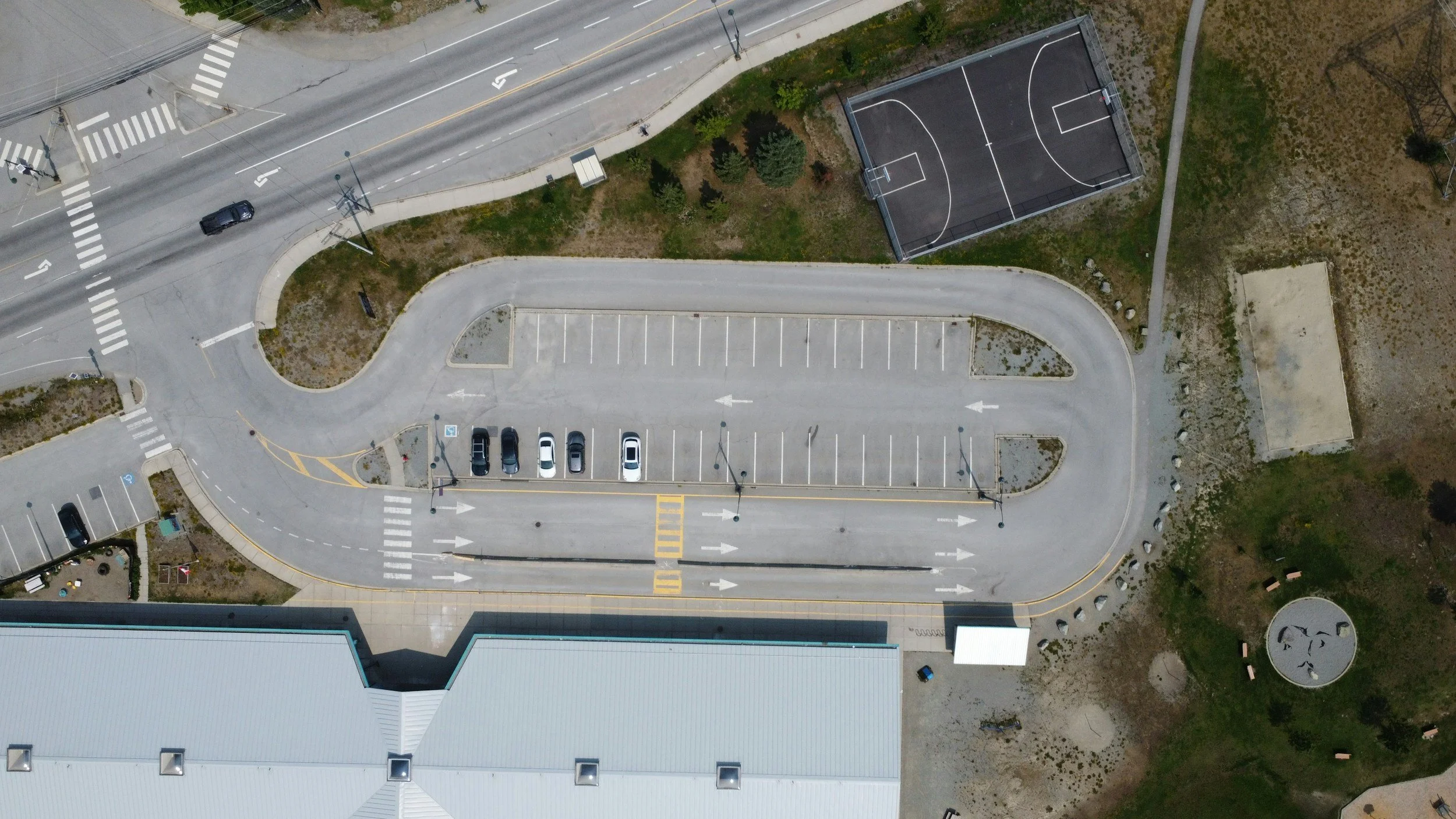 Kuva ilmasta, jossa on pysäköintialue, kadunpätkä ja koripallokenttä.