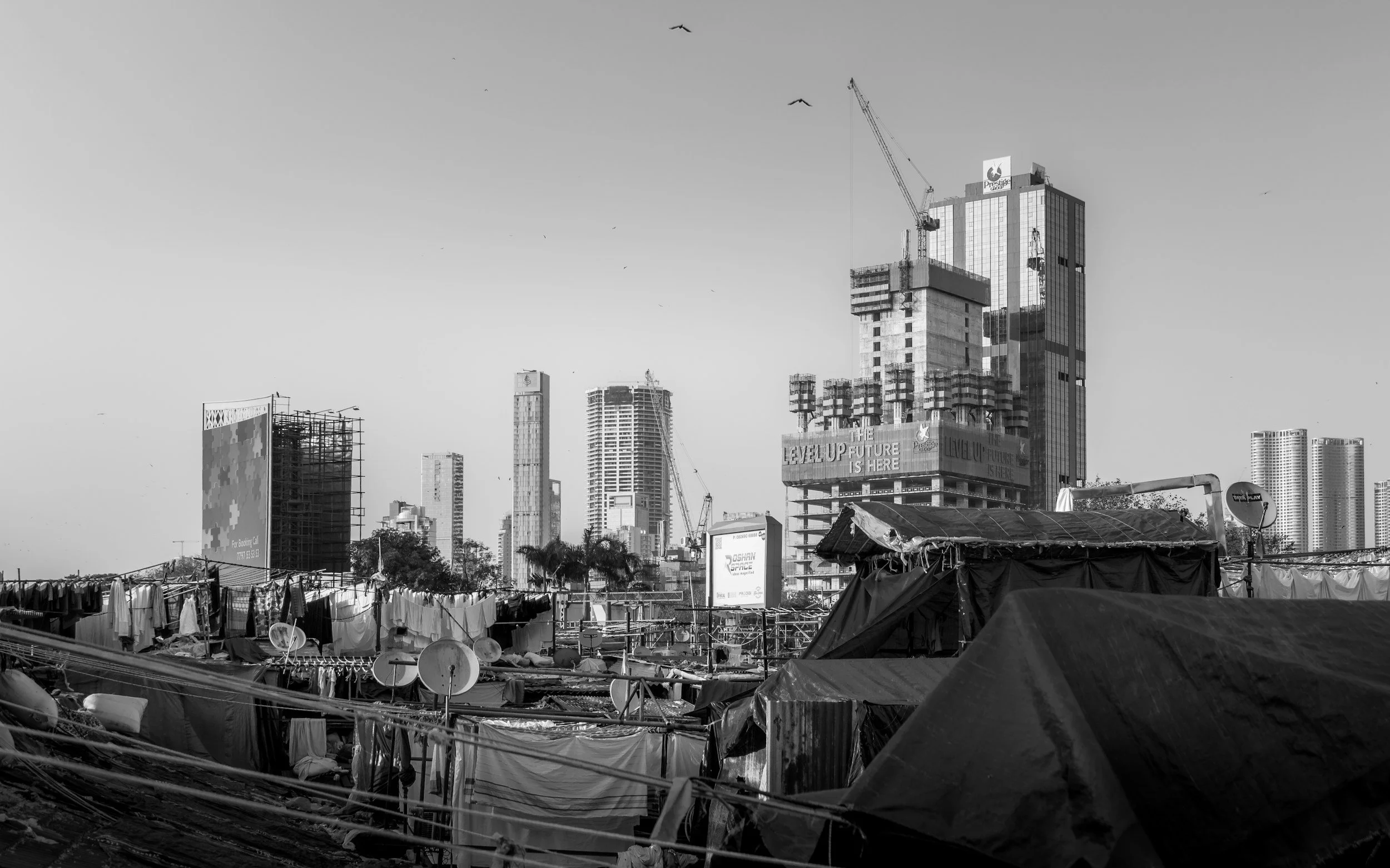 Kuvassa on rakennustyömaa korkeissa kerrostaloissa ja telakkalaiturilla, jossa on vanhoja katoksia ja kuivuvia vaatteita.